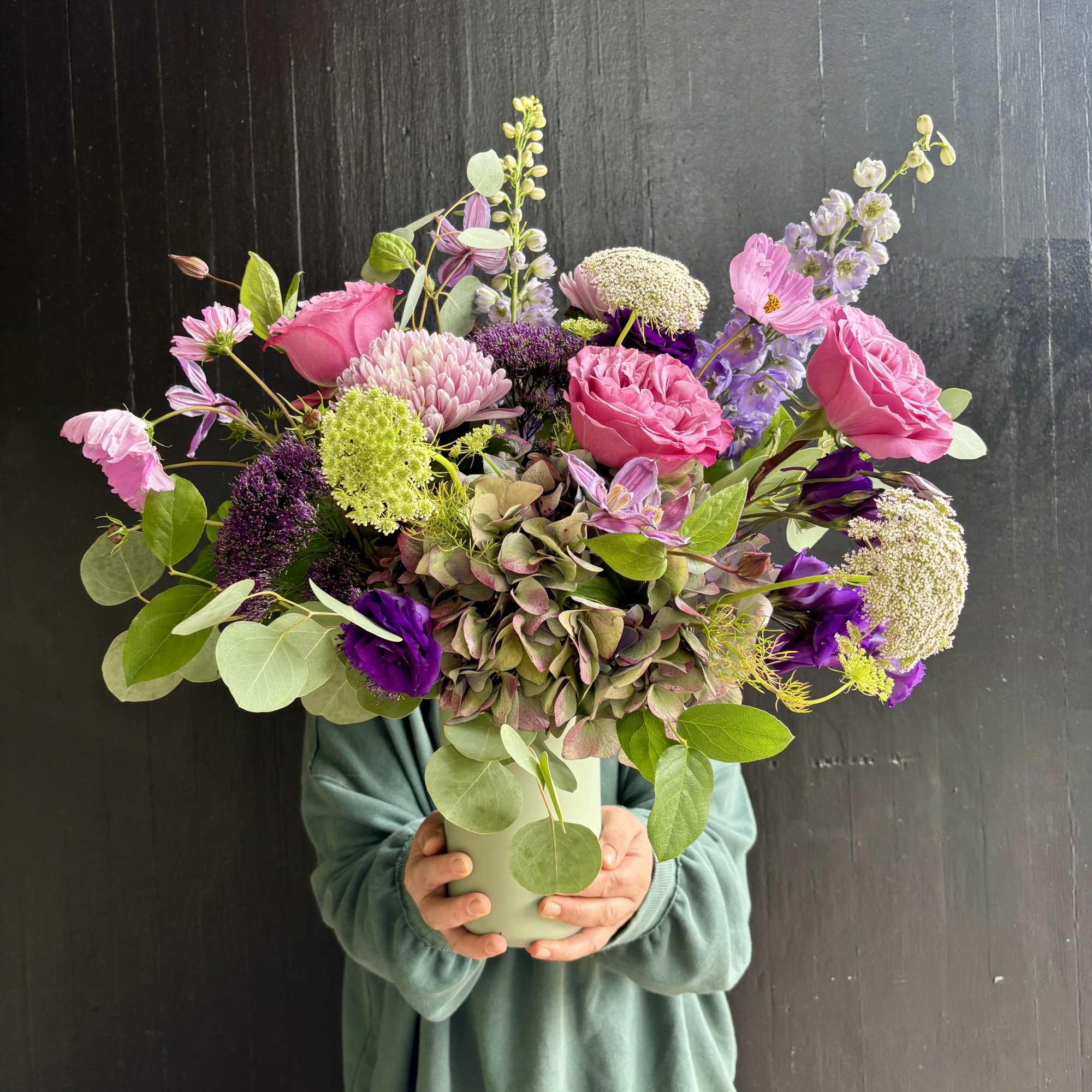Handheld bouquet of pink and purple flowers in a pale green vase