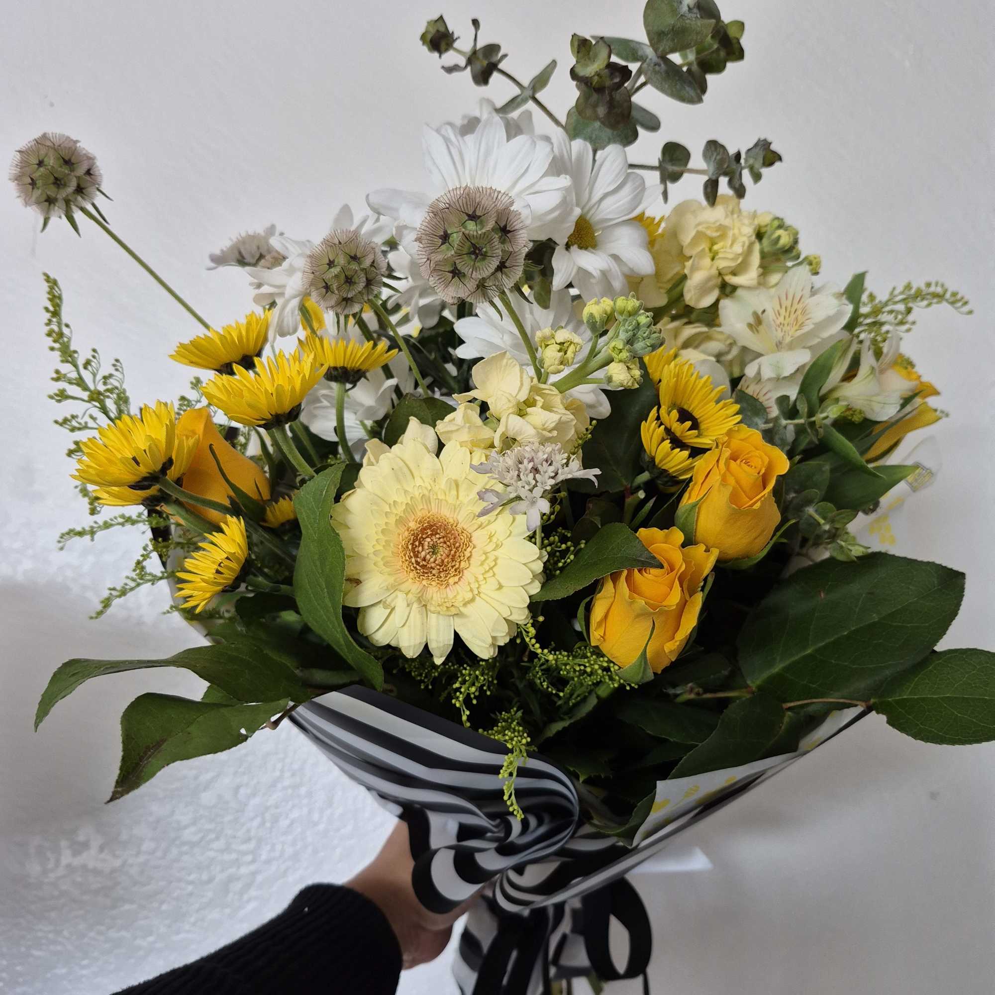 Bouquet of yellow roses, white daisies, and pale blooms wrapped in striped paper