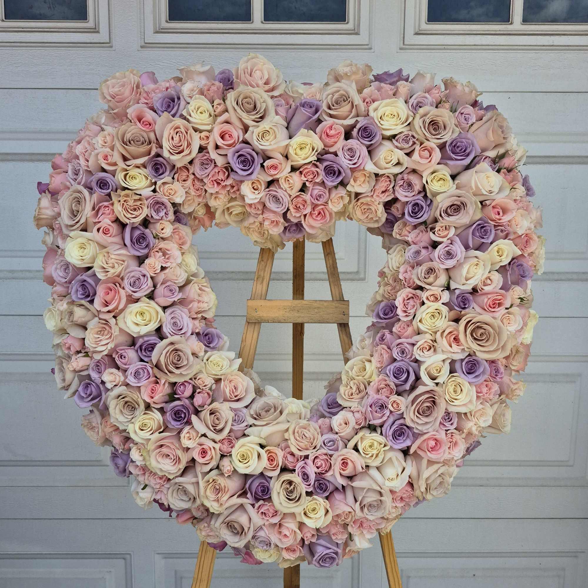 Heart-shaped rose wreath on a wooden easel in pink and lavender tones