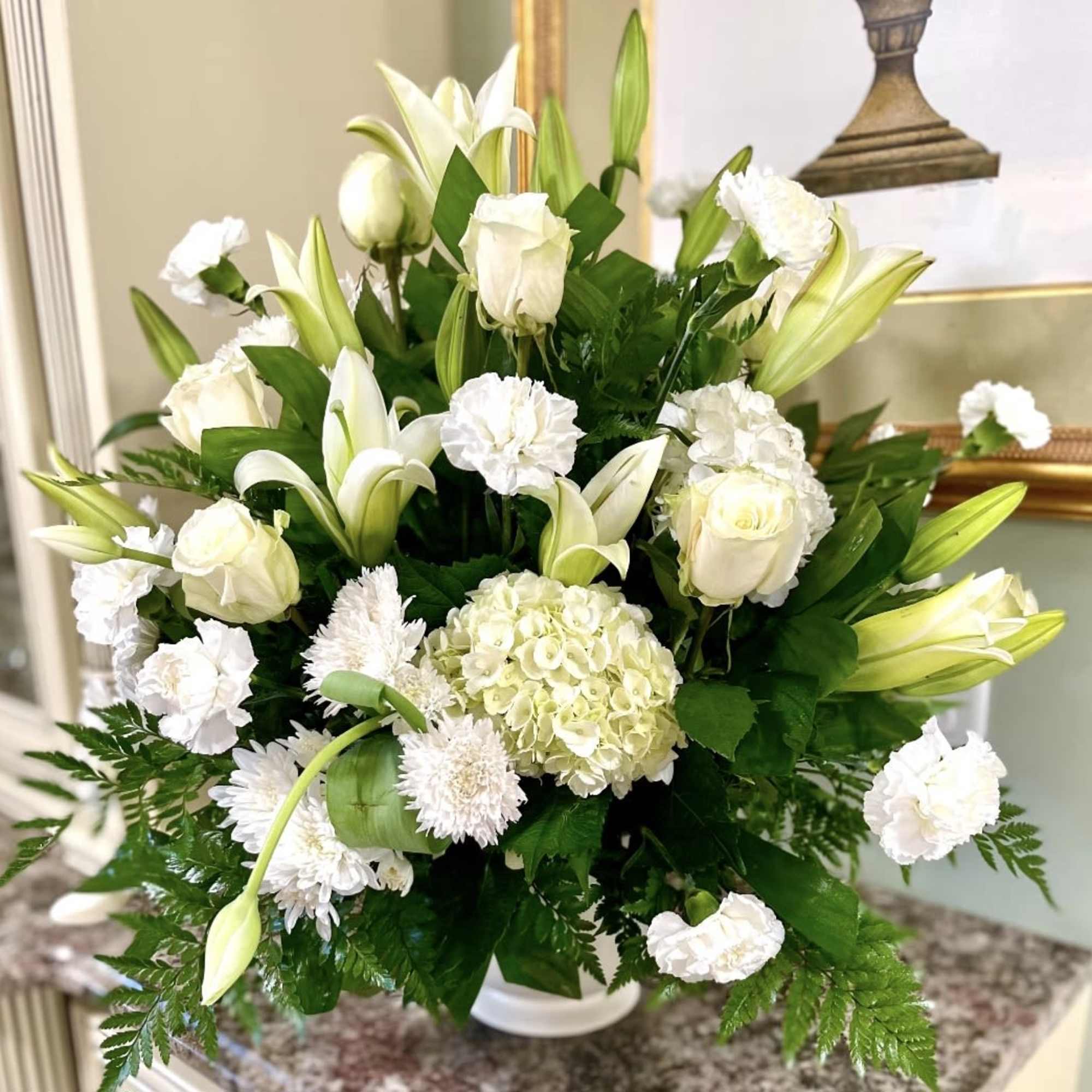 White floral arrangement with lilies, roses, hydrangea, and carnations in a vase