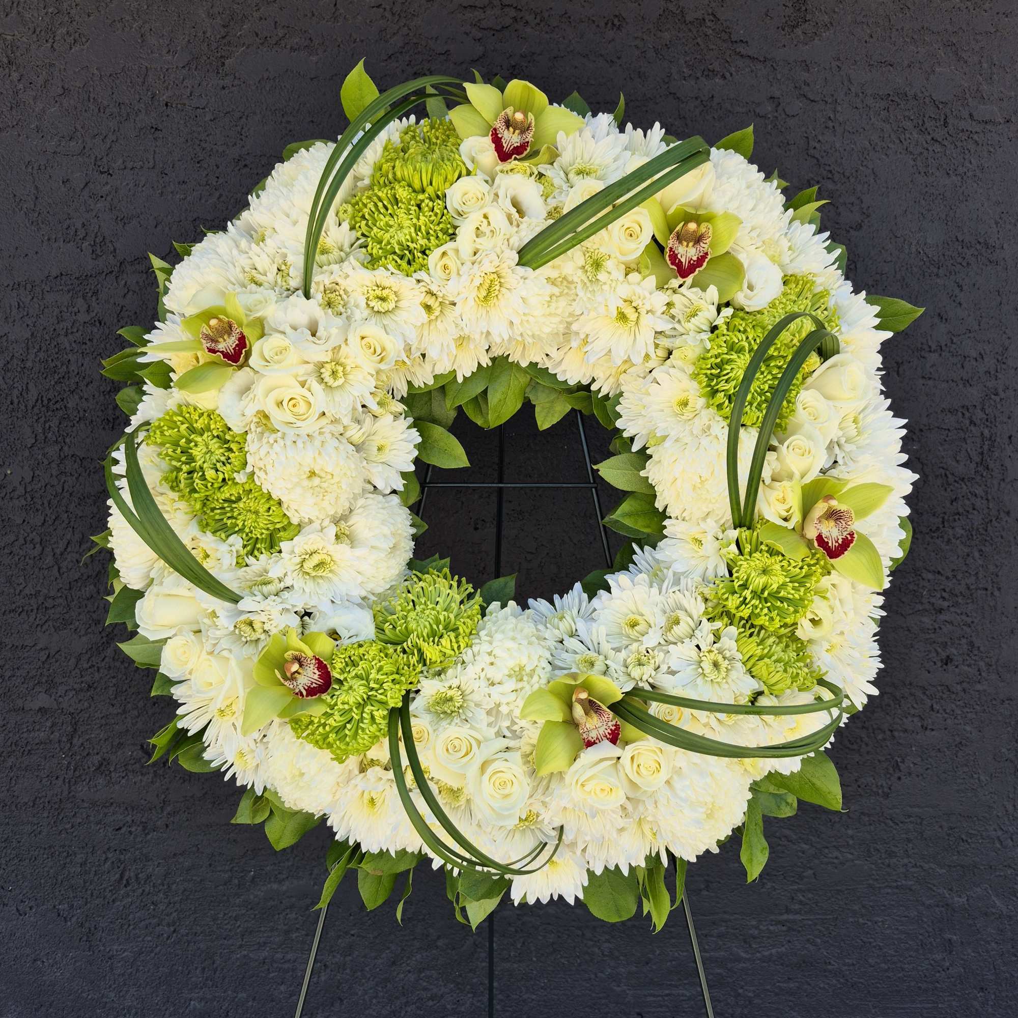 White and green floral wreath on a stand with orchids and chrysanthemums