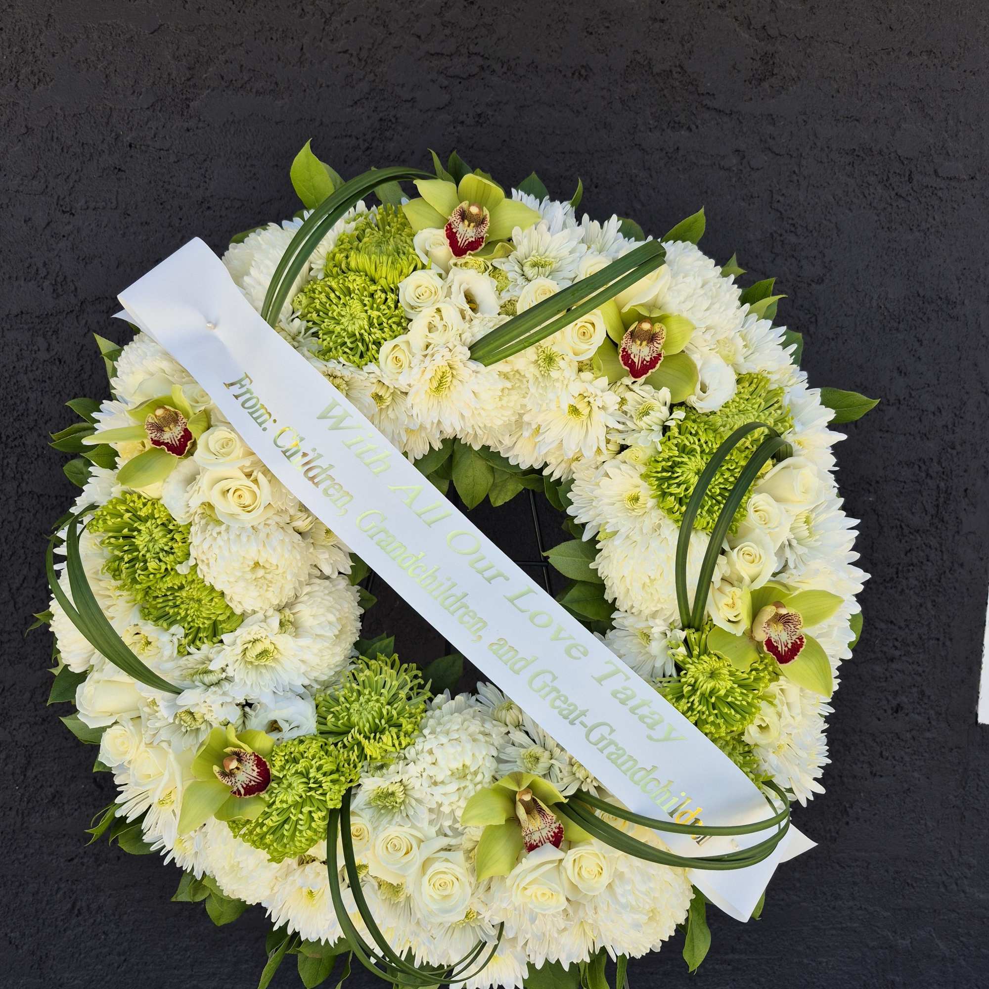White and green funeral wreath with orchids and a ribbon tribute