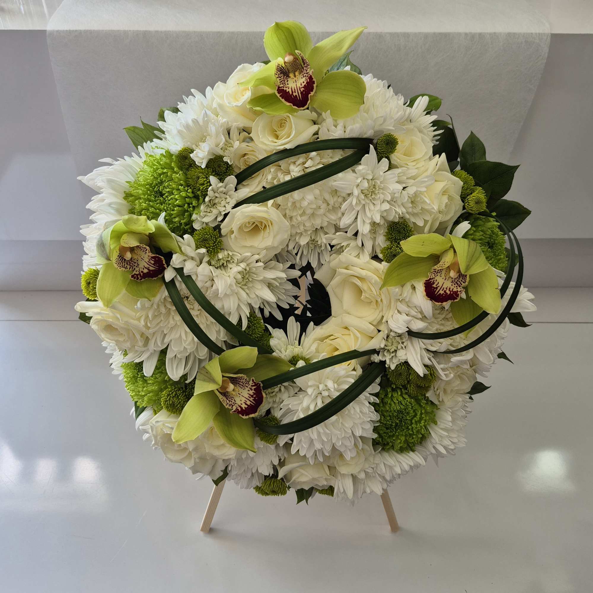 Round white floral arrangement with green orchids and roses on a stand