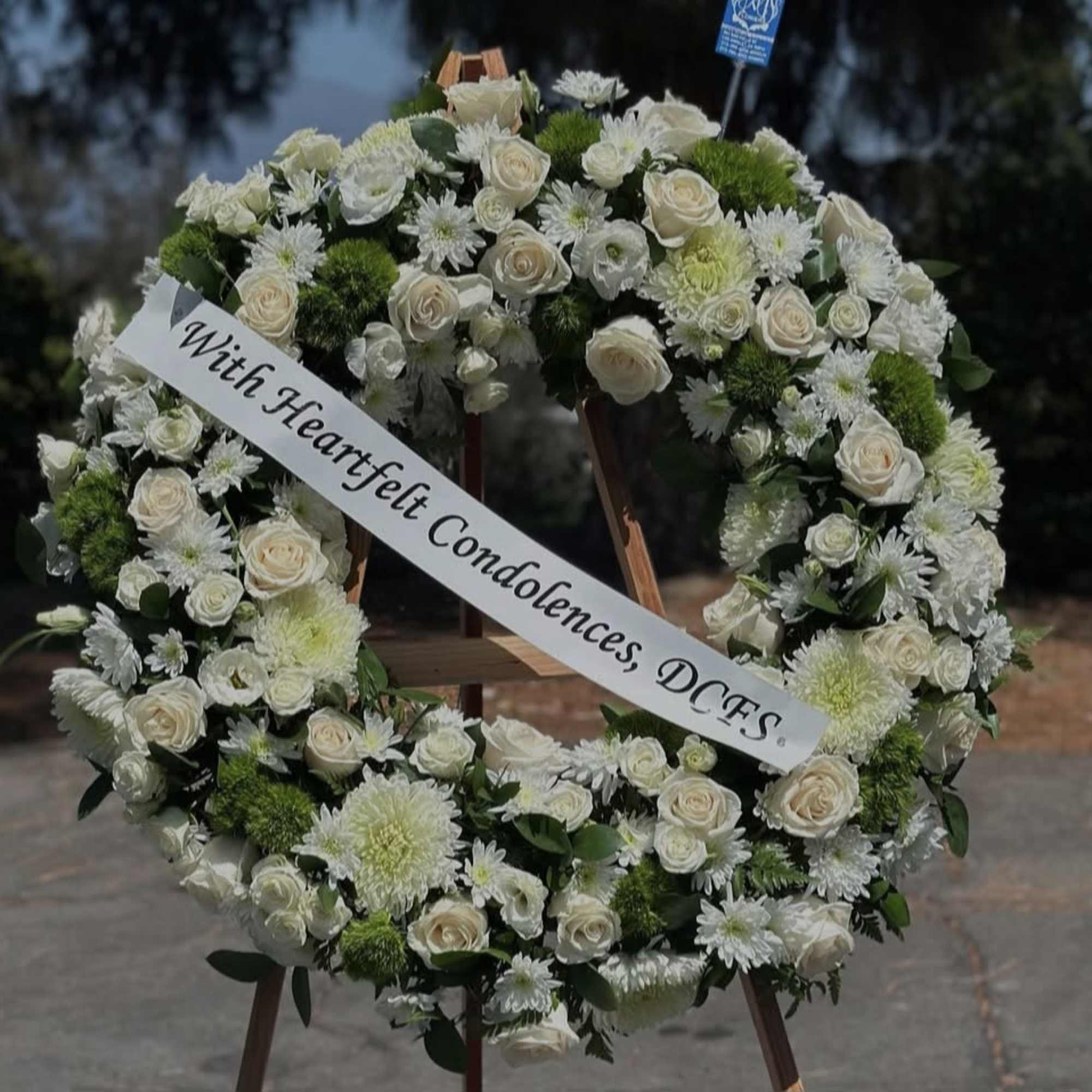 White floral sympathy wreath on an easel with a condolence ribbon