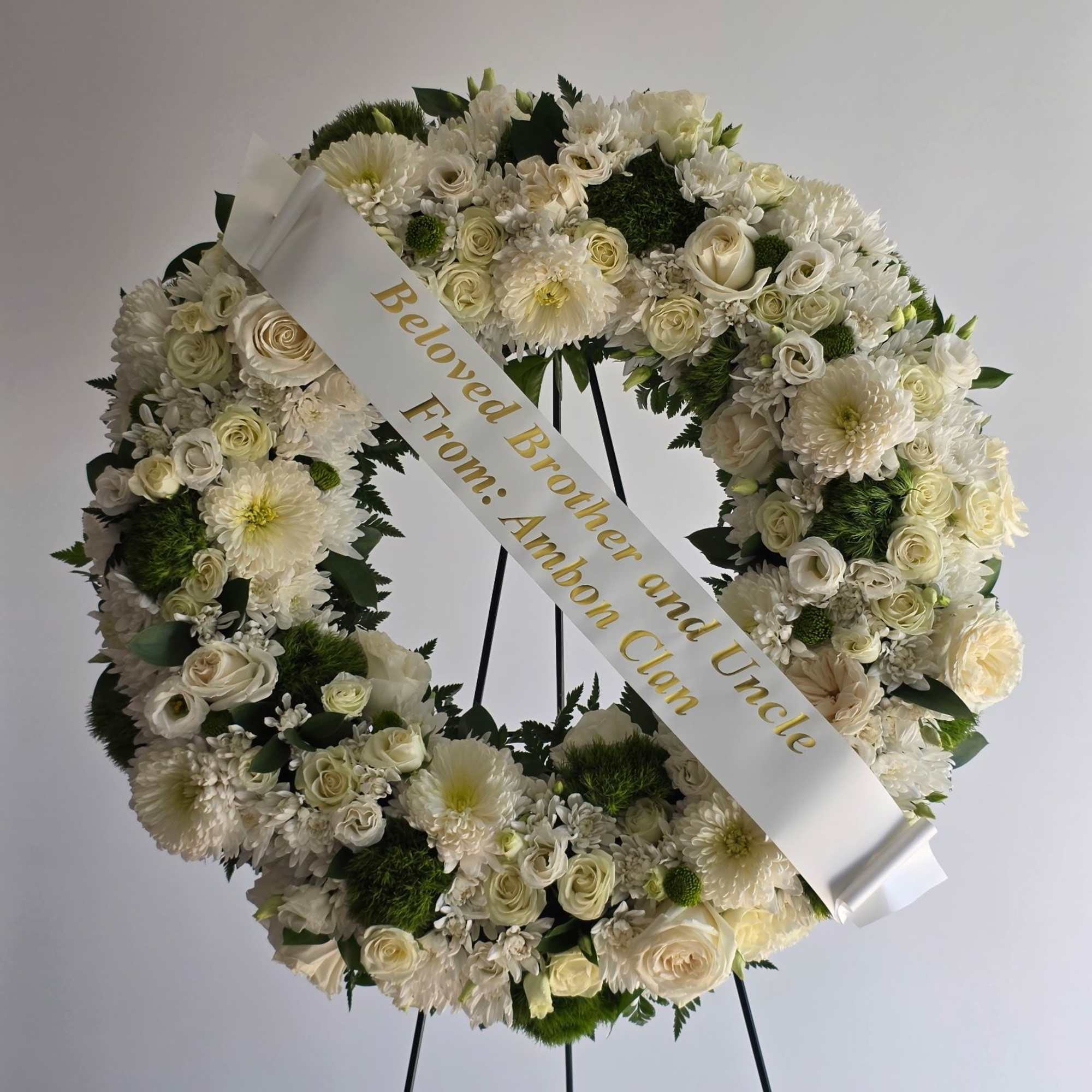 White floral funeral wreath with a memorial ribbon on a stand