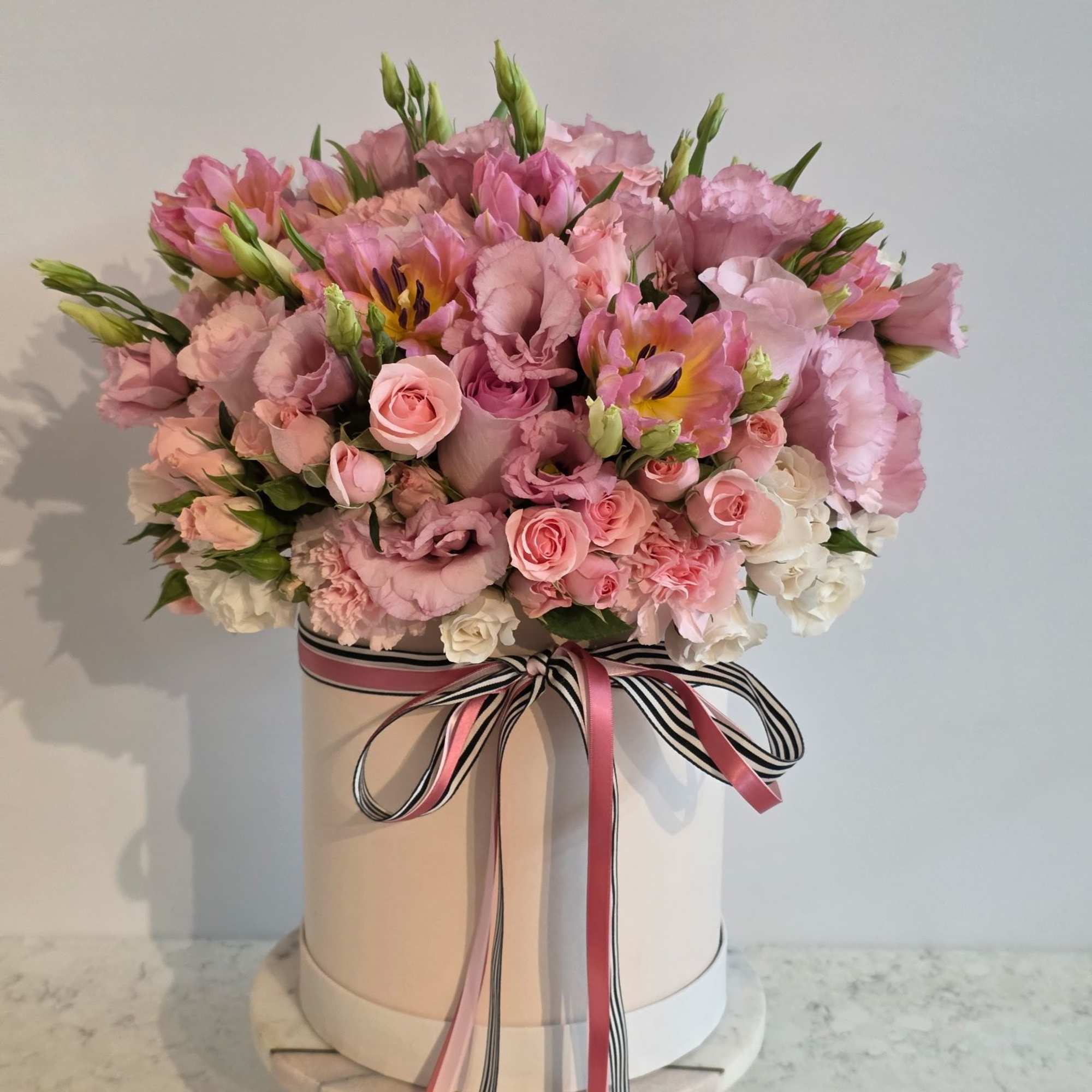 Pink floral arrangement in a round hat box with ribbon bow