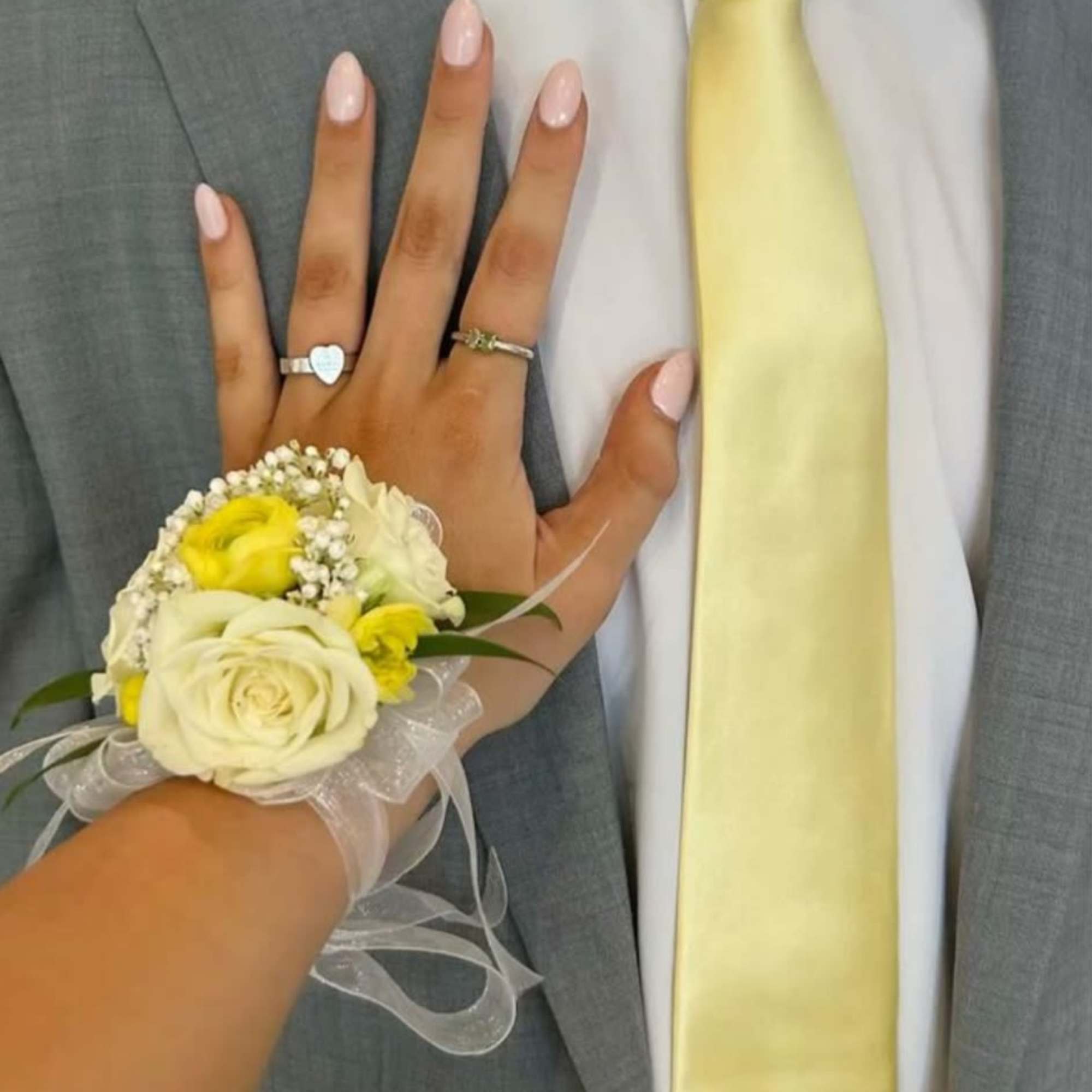 A delicate wrist corsage in soft cream-white roses and bright yellow accent