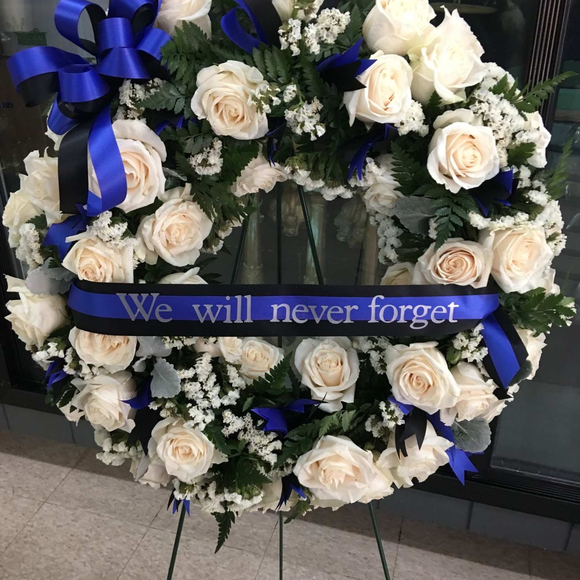 White rose funeral wreath with blue ribbon on an easel