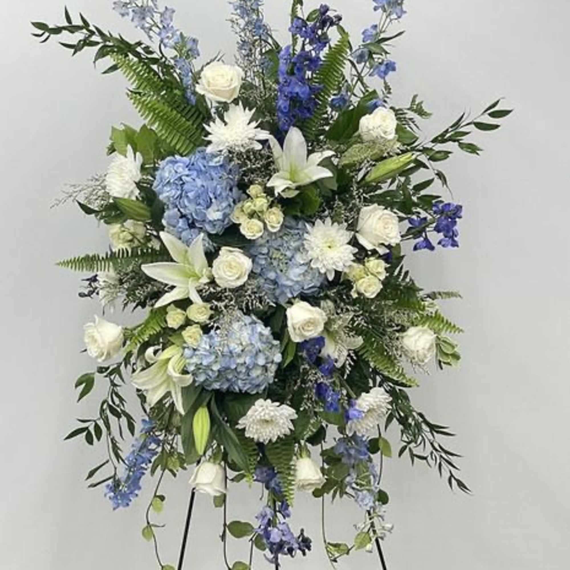 Large standing floral spray with blue and white flowers on a black easel