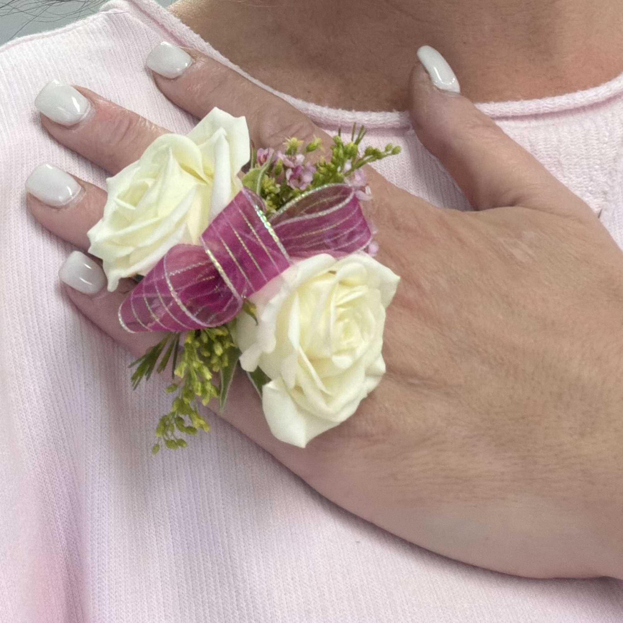 White rose corsage with pink ribbon on a hand