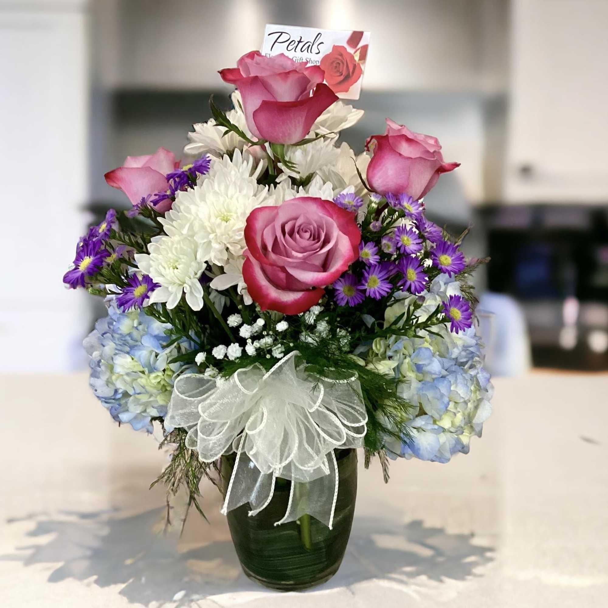 Pink roses and white flowers arranged in a glass vase with a white bow