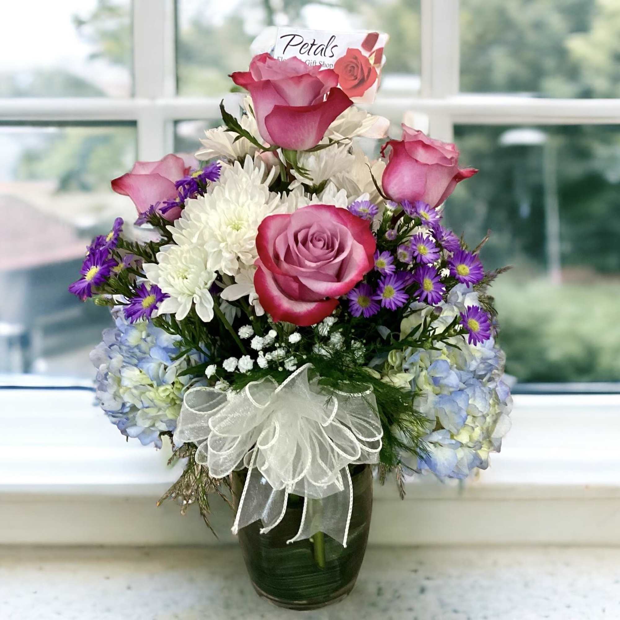 Pink roses and white flowers in a glass vase with a white bow