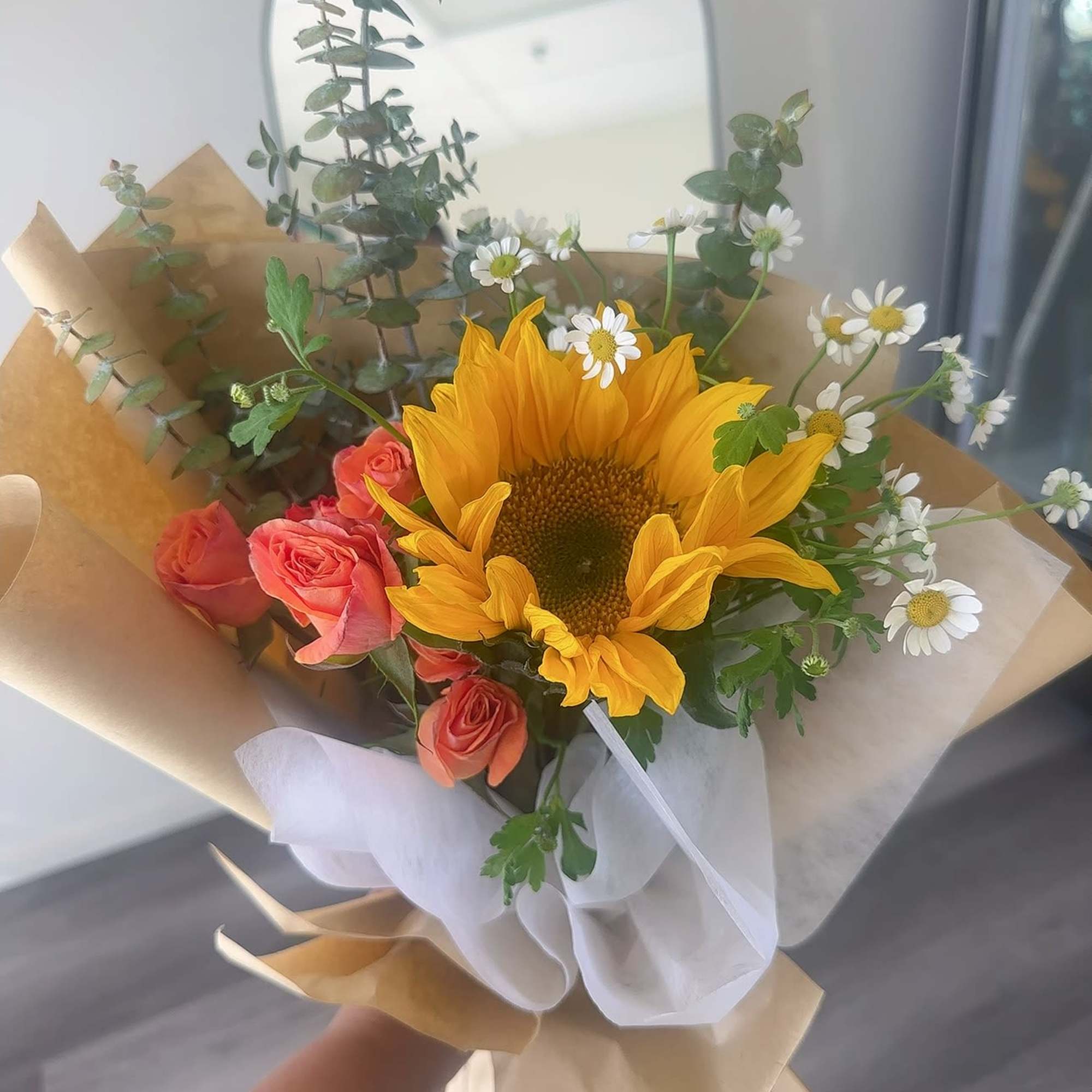 Bouquet with a sunflower, coral roses, and small white daisies