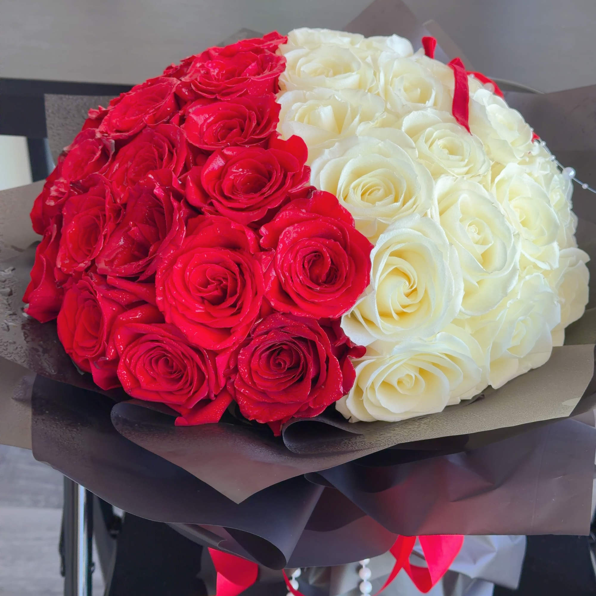 Red and white rose bouquet wrapped in dark paper, photo 3 of 4