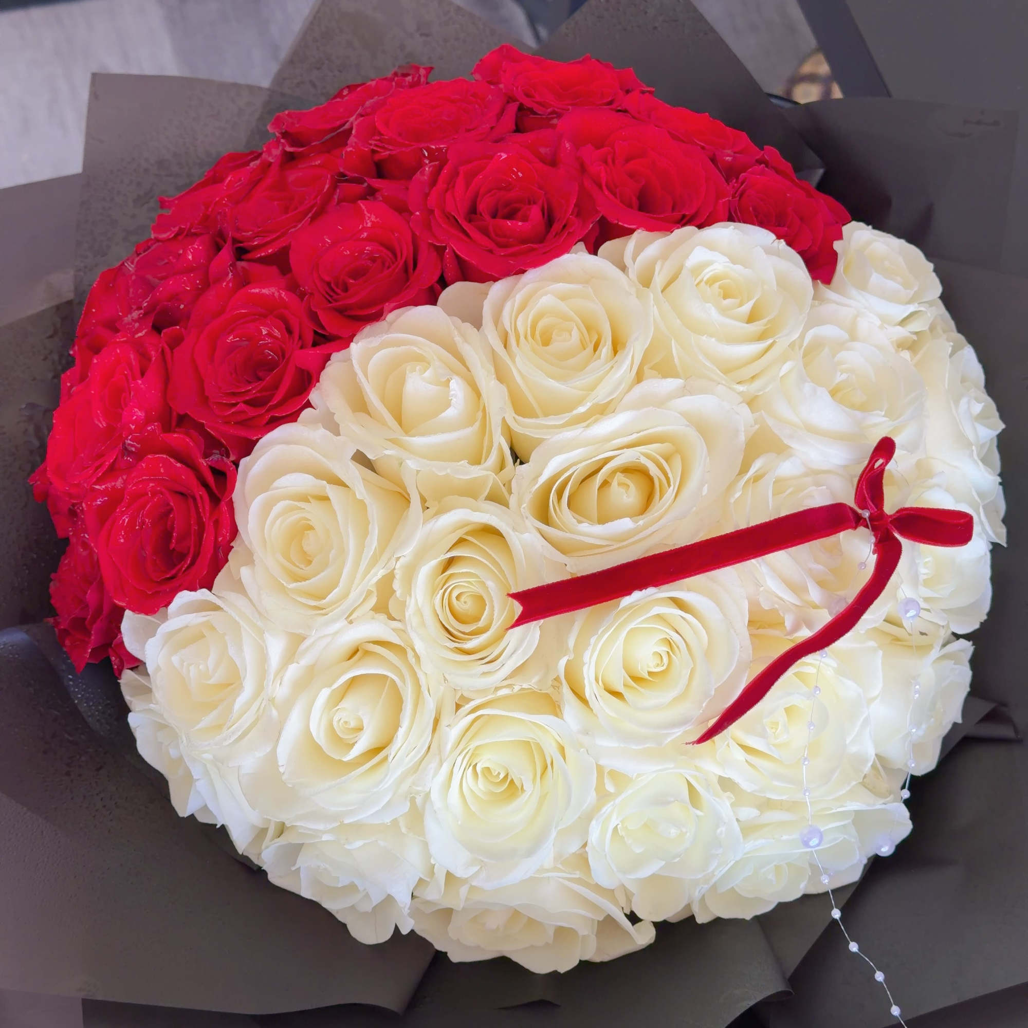 Round bouquet of red and white roses wrapped in dark paper, photo 4 of 4