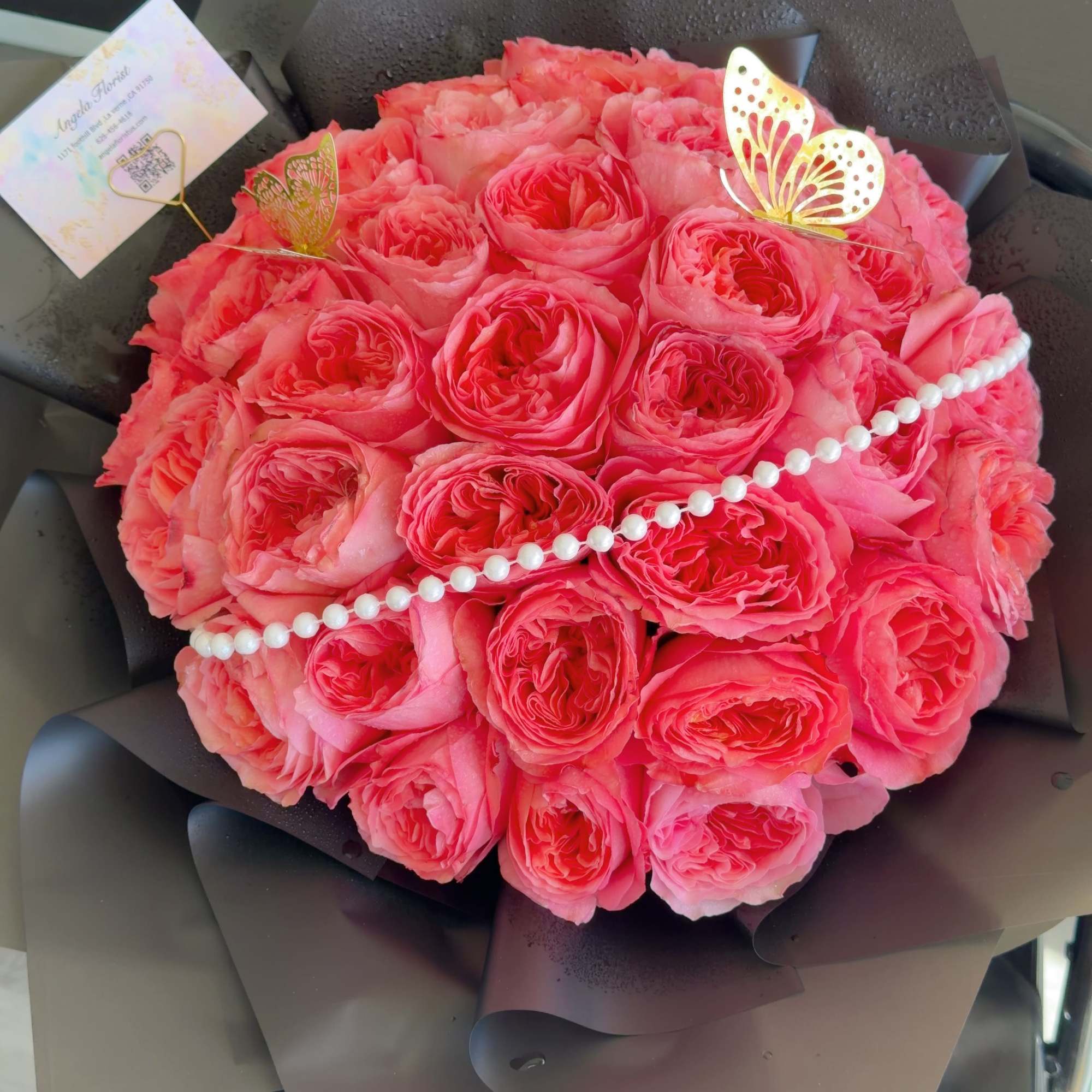 Round bouquet of pink roses wrapped in dark paper with pearl trim