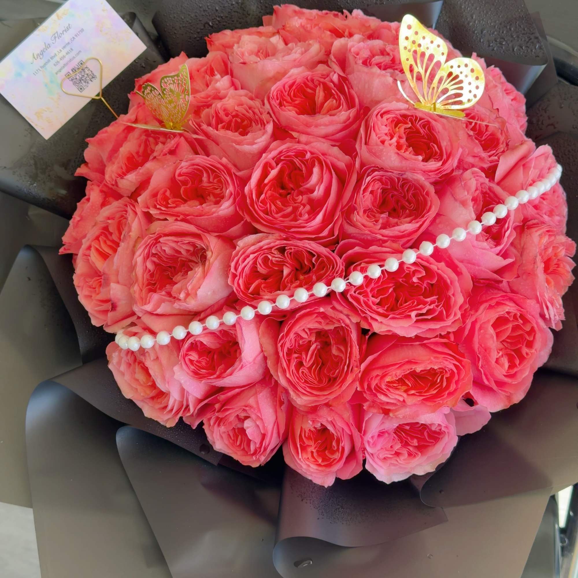 Round bouquet of pink roses wrapped in dark paper with pearl trim, photo 4 of 4
