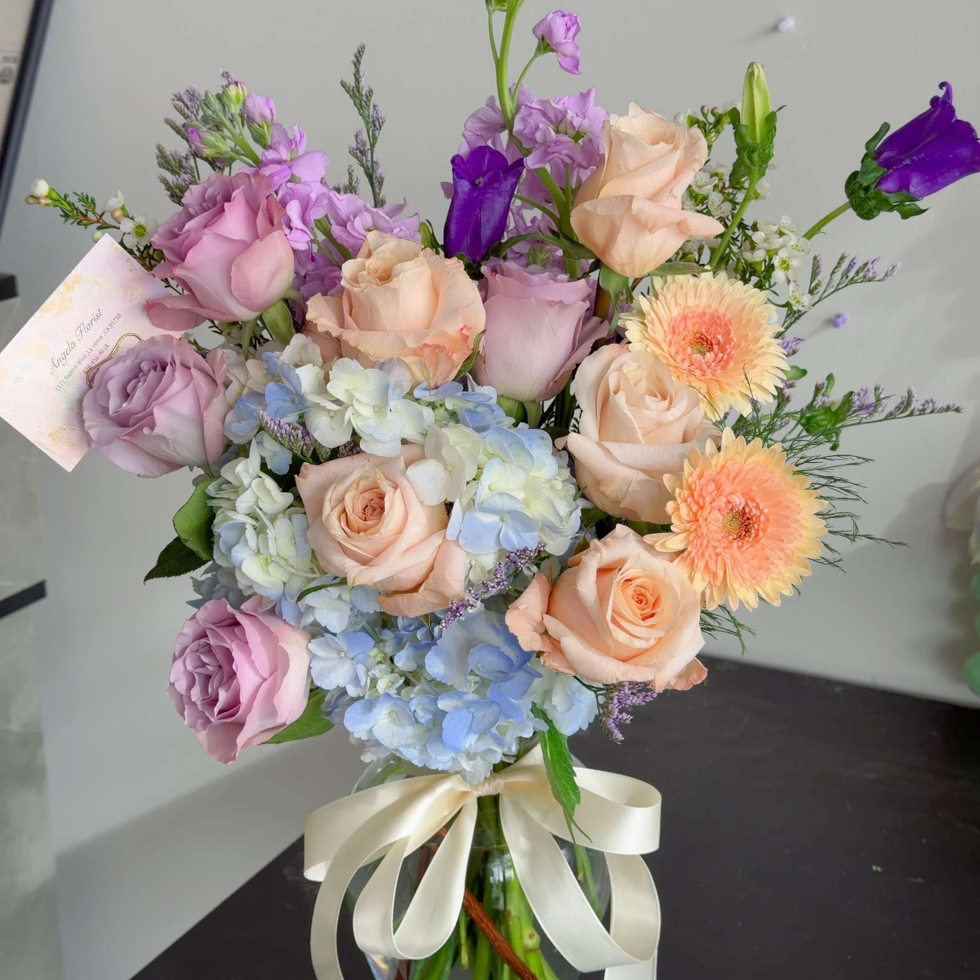 Bouquet of pastel roses, hydrangeas, and purple blooms in a glass vase