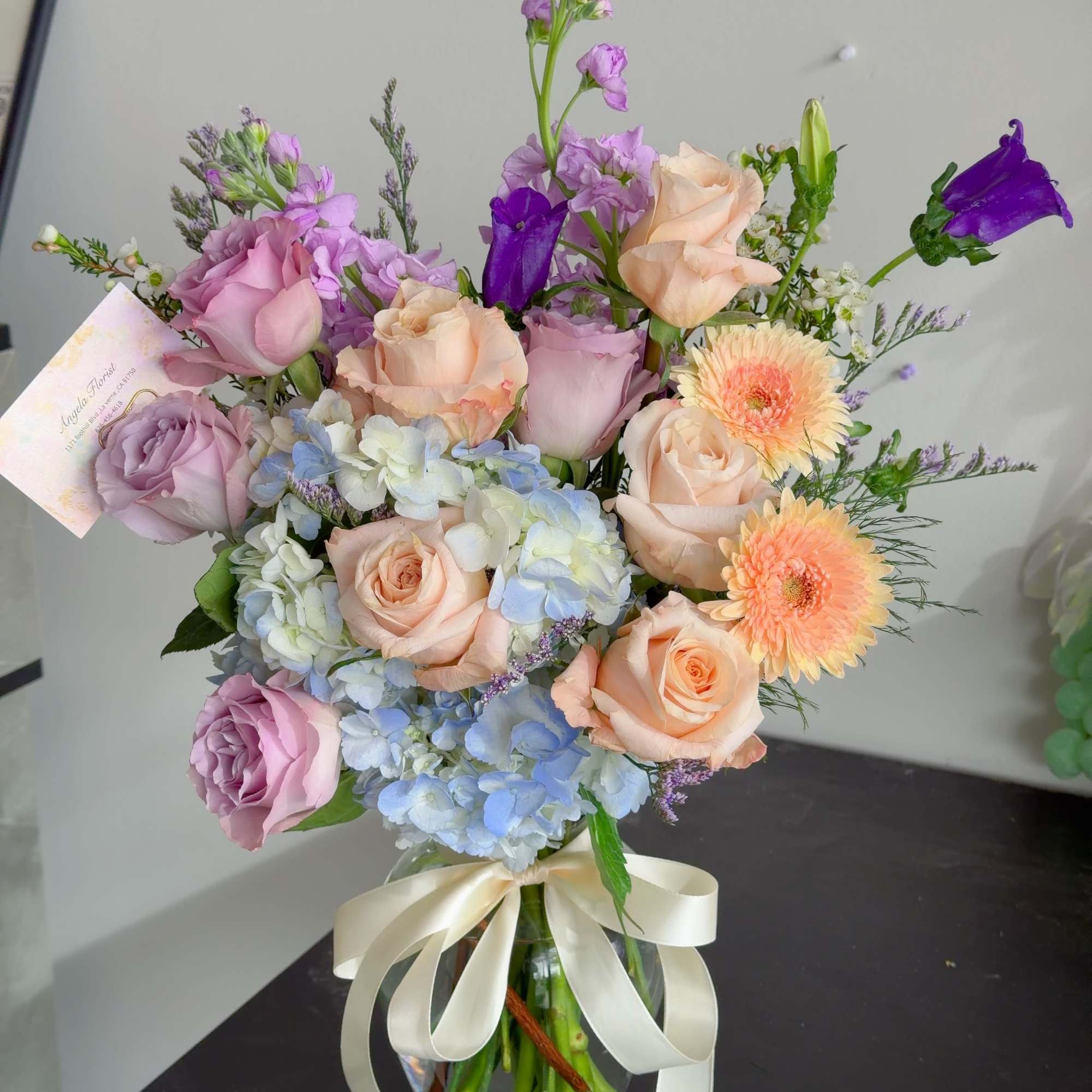 Pastel bouquet of roses, hydrangeas, and gerbera daisies in a glass vase with ribbon