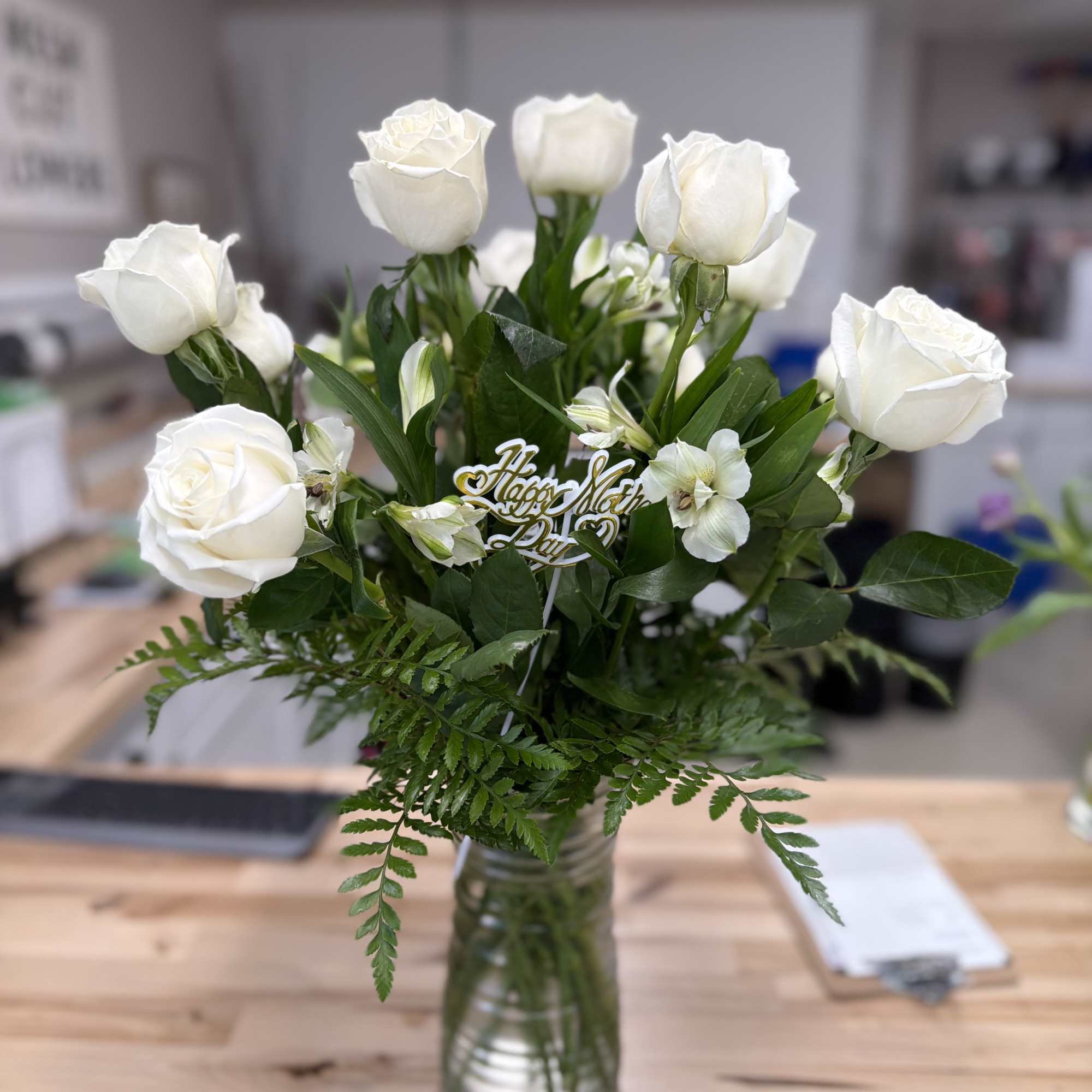 White roses and small white flowers in a glass vase with greenery