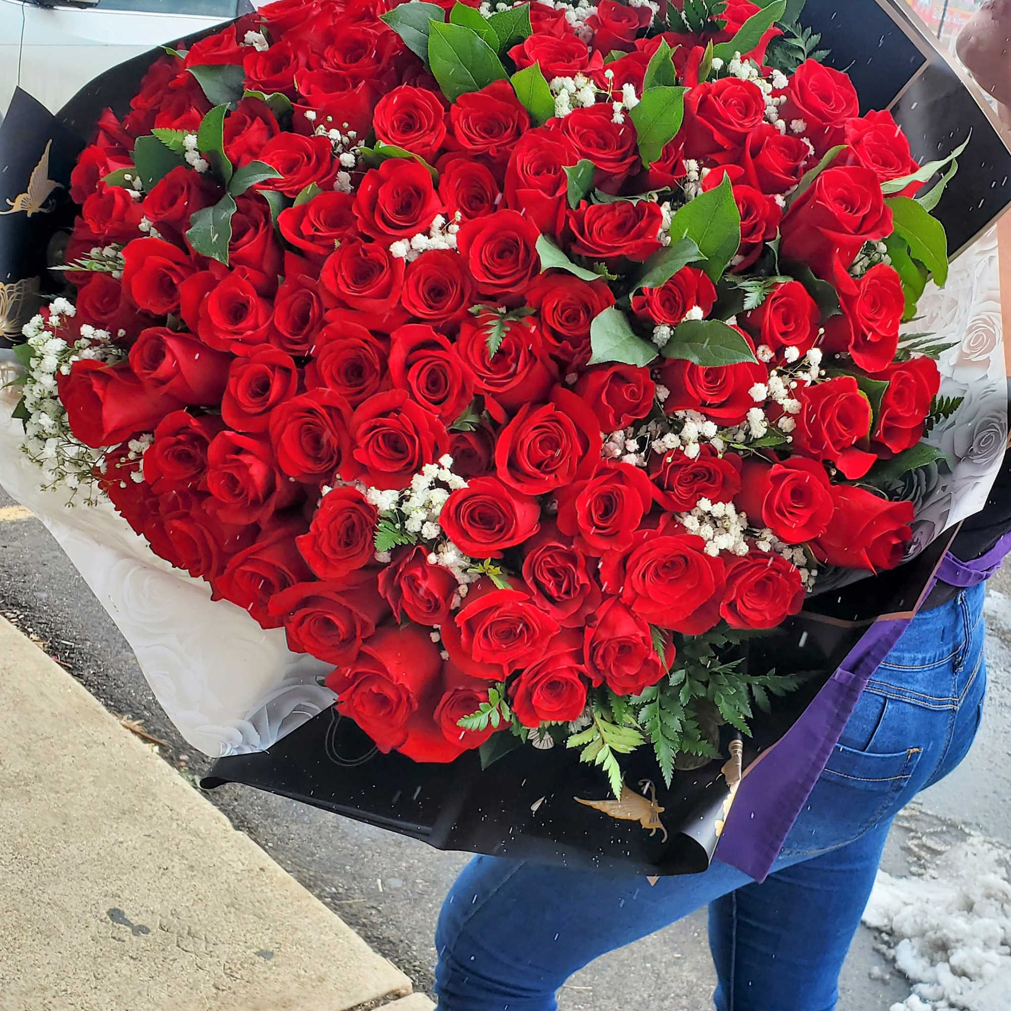 Large bouquet of red roses with white filler flowers and green leaves