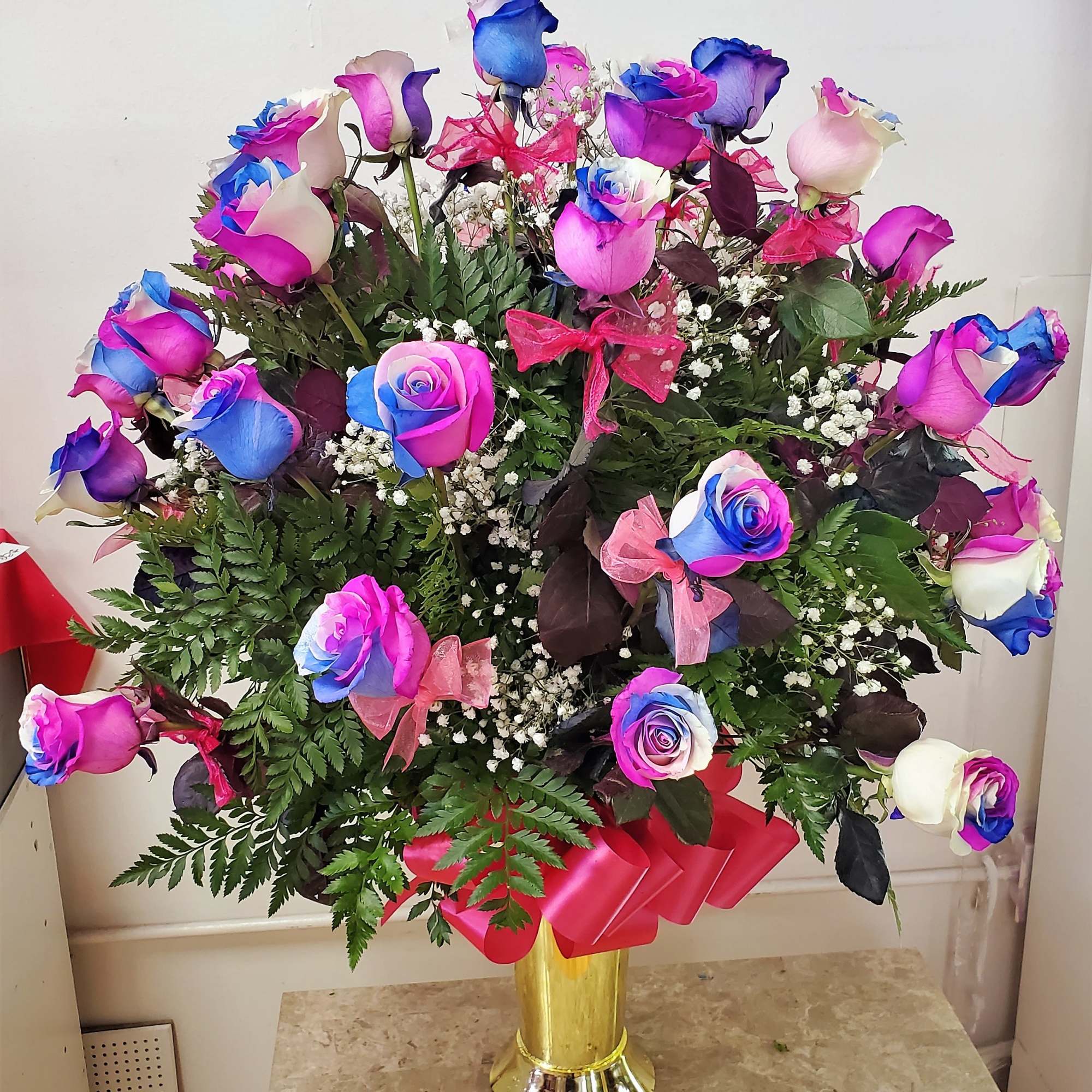 Bouquet of multicolored roses in a gold vase with pink ribbon