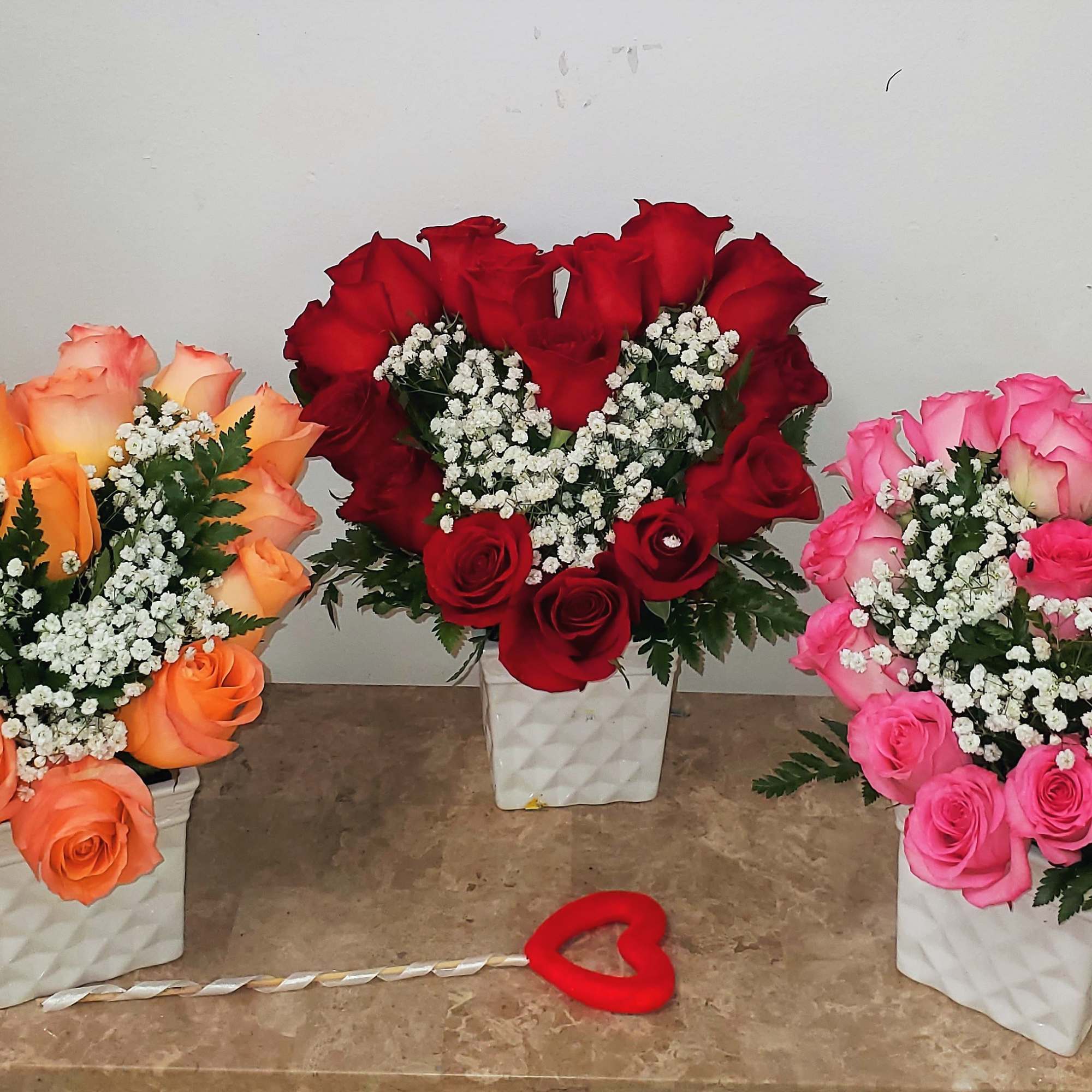 Three rose arrangements in white square vases with baby’s breath