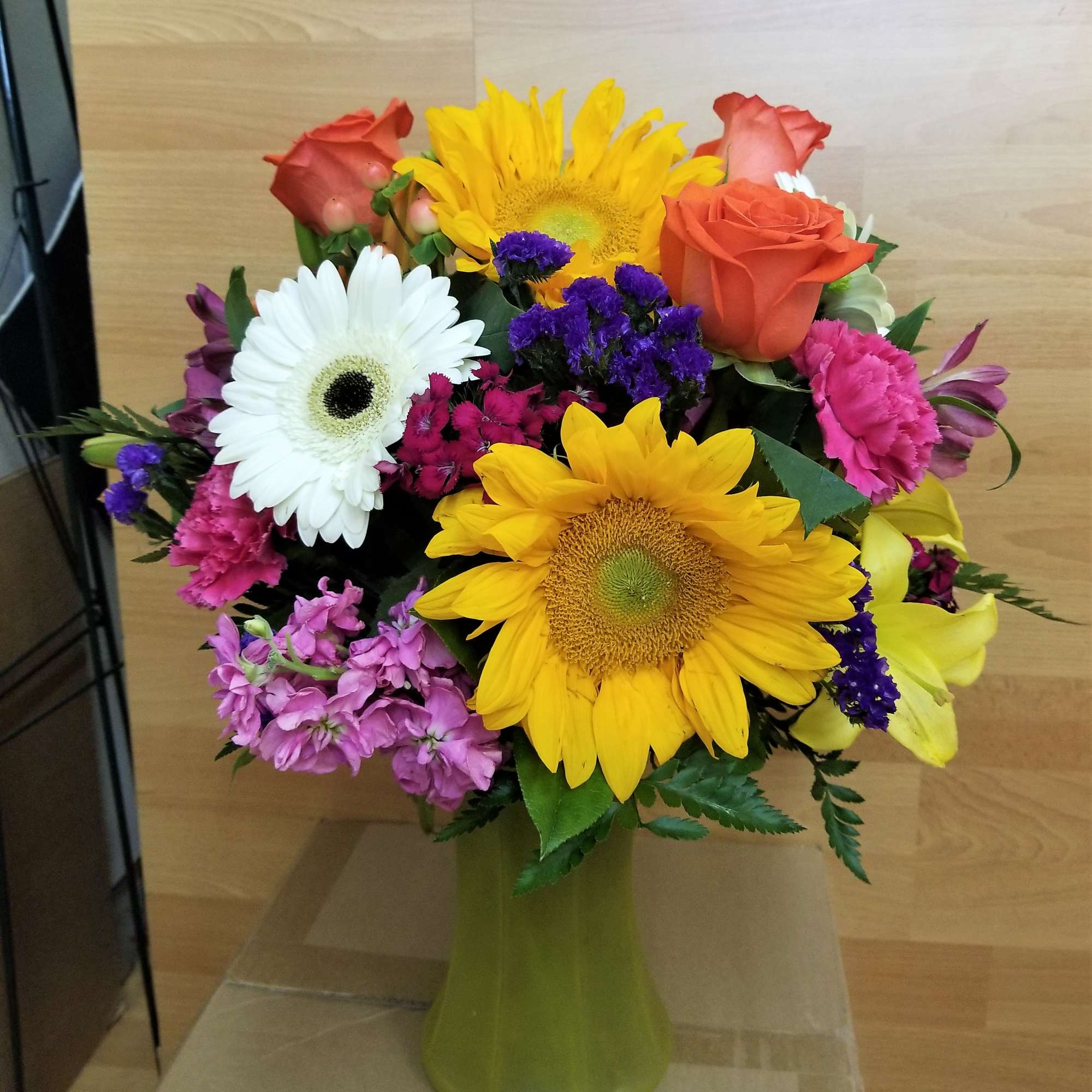 Colorful bouquet with sunflowers, roses, and daisies in a green vase
