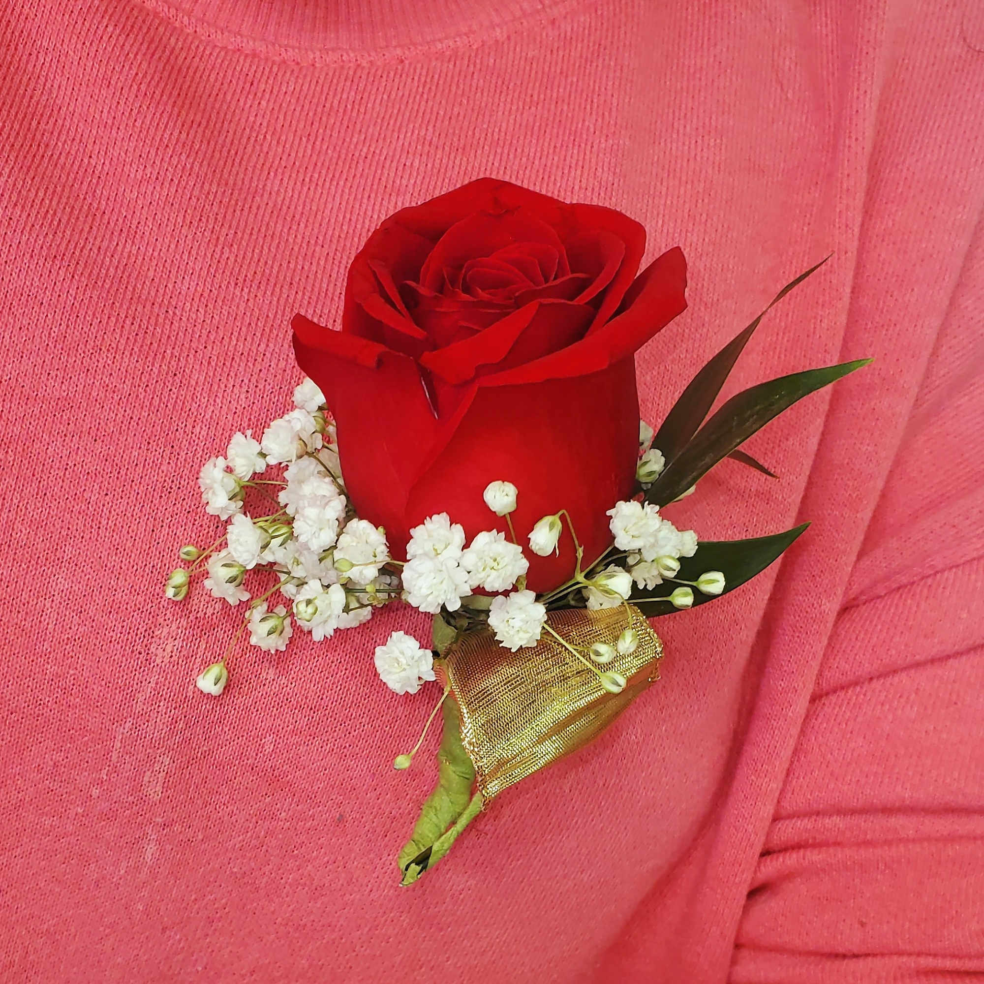 Red rose boutonniere with white baby's breath on pink fabric