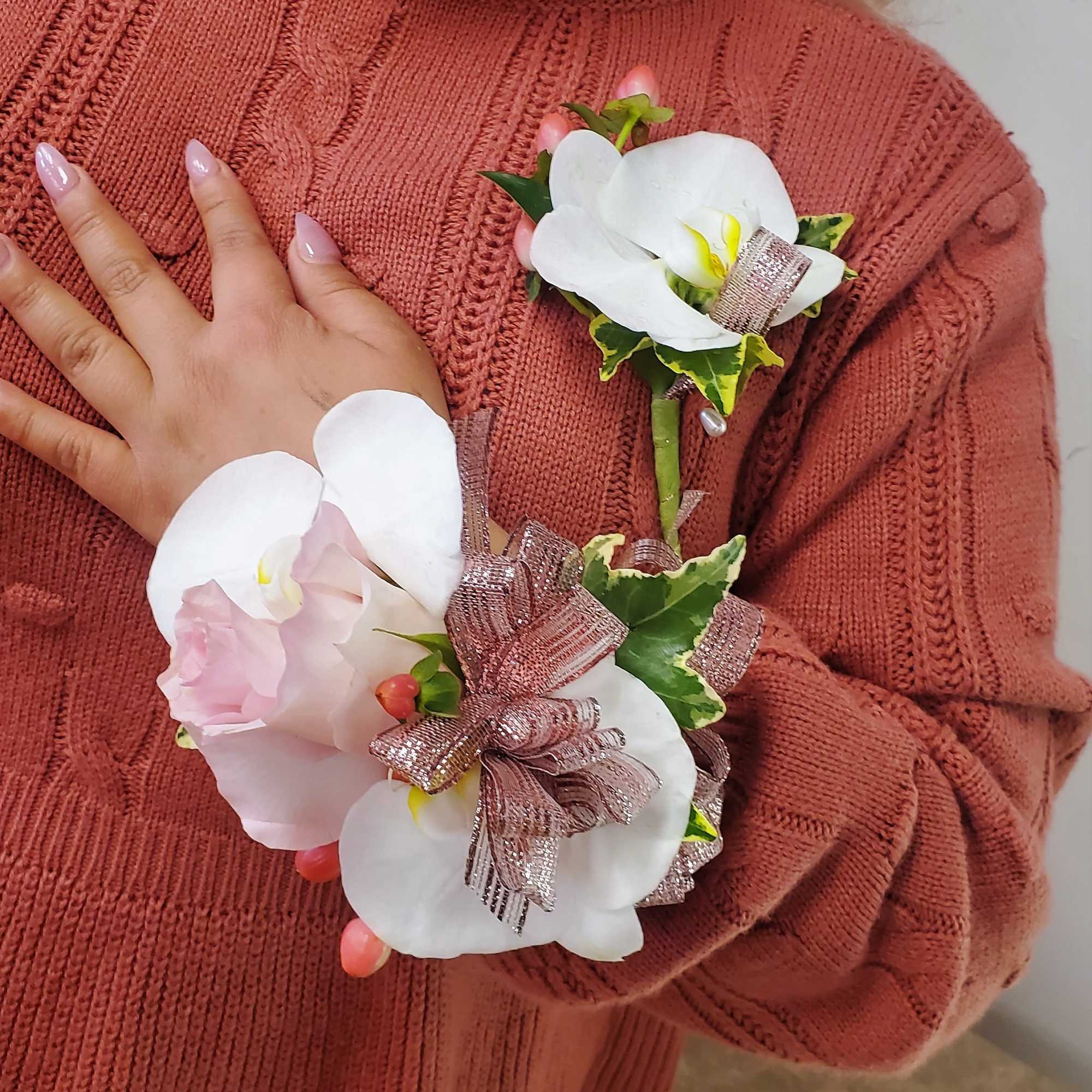 White orchid corsage with pink ribbon accents worn on a sweater