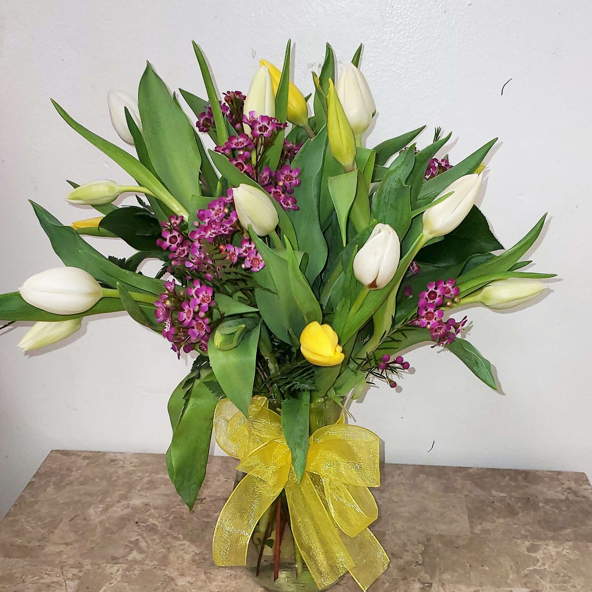 Bouquet of white and yellow tulips with purple filler in a glass vase