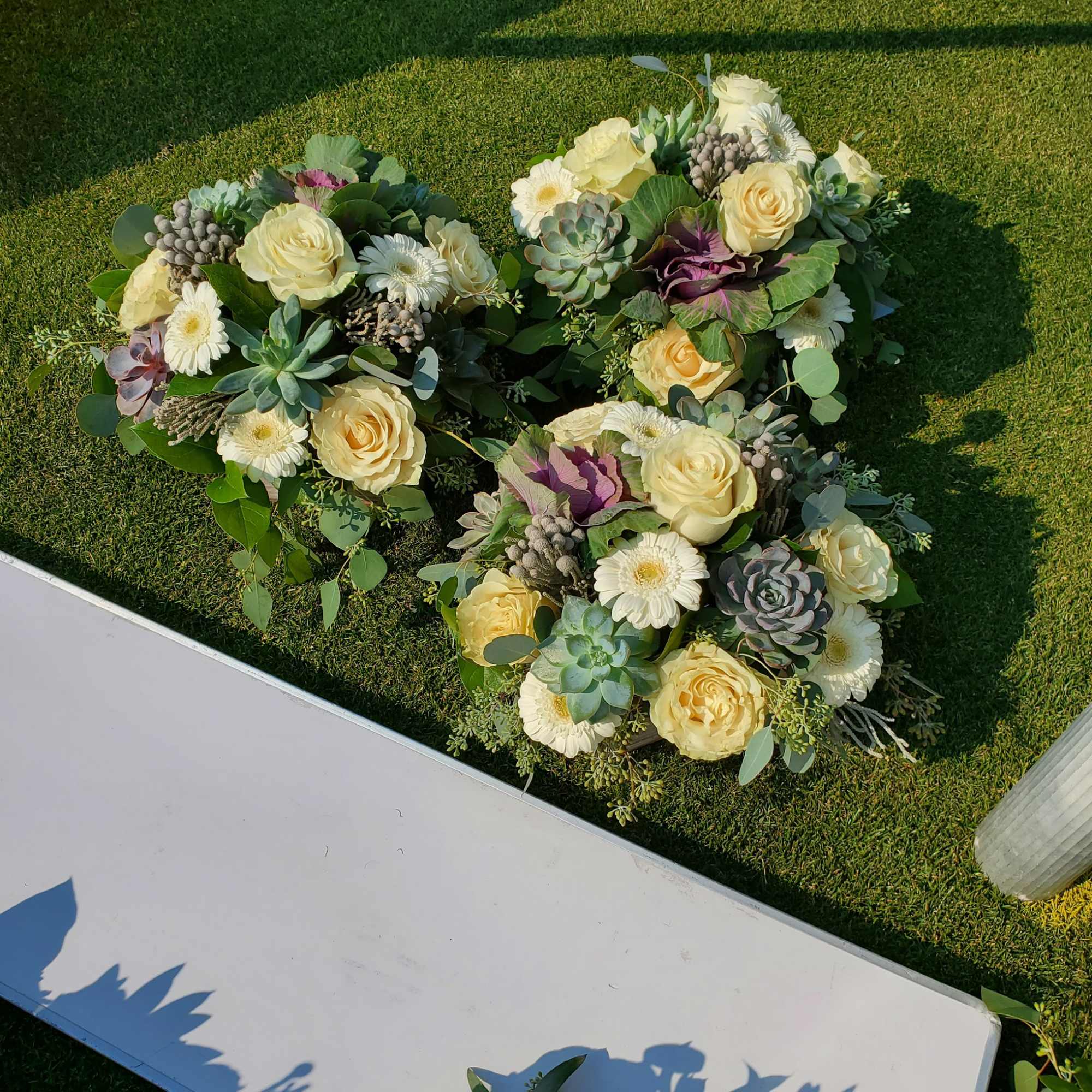Heart-shaped floral arrangement with cream roses and white daisies on grass