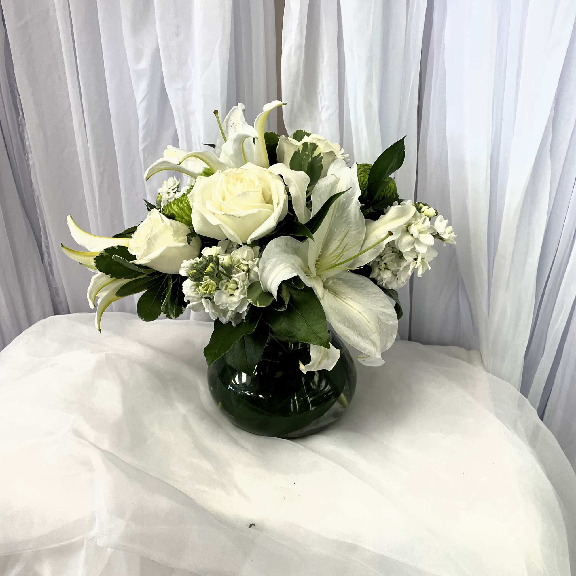 White roses and lilies arranged in a dark glass vase