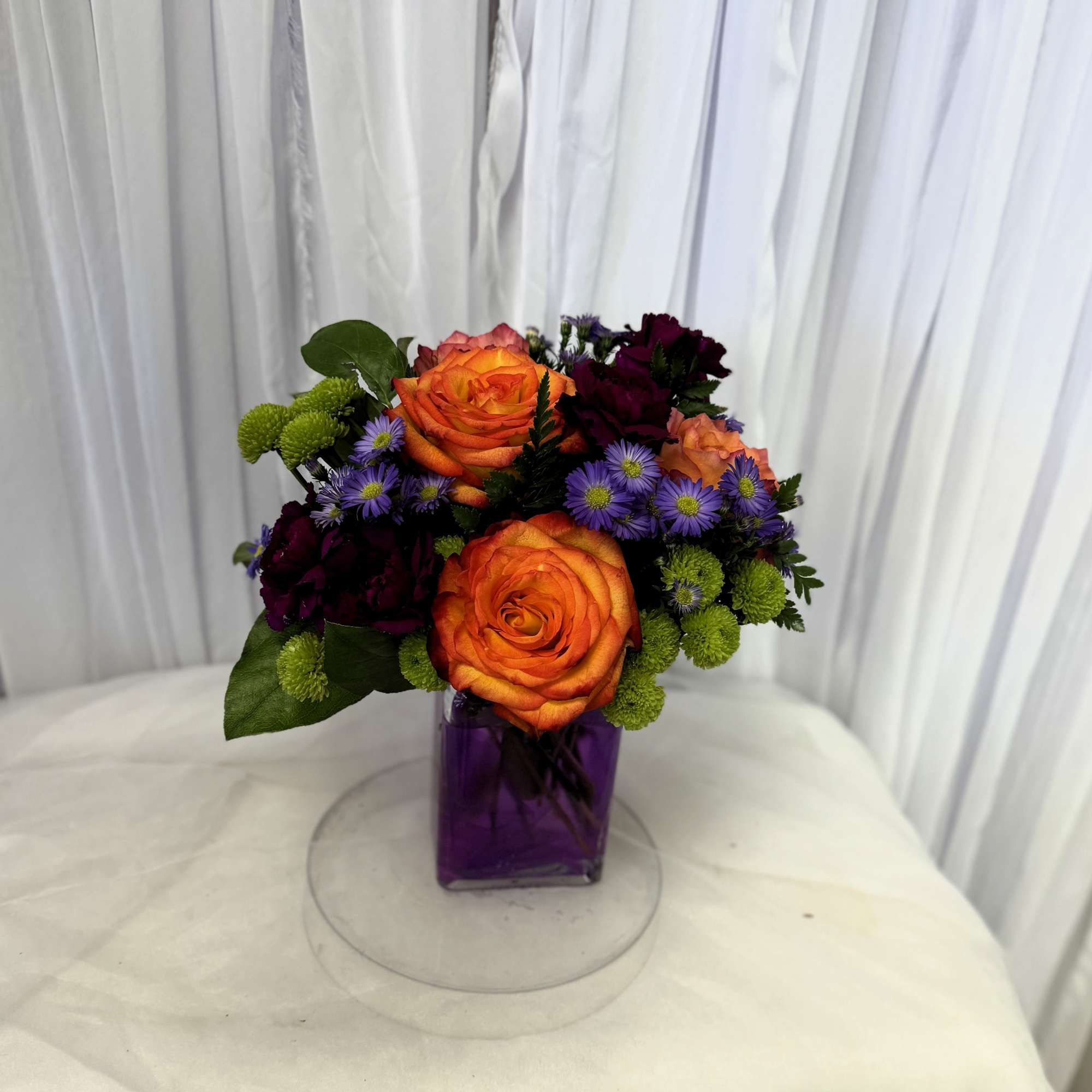 Orange roses and purple flowers arranged in a purple vase