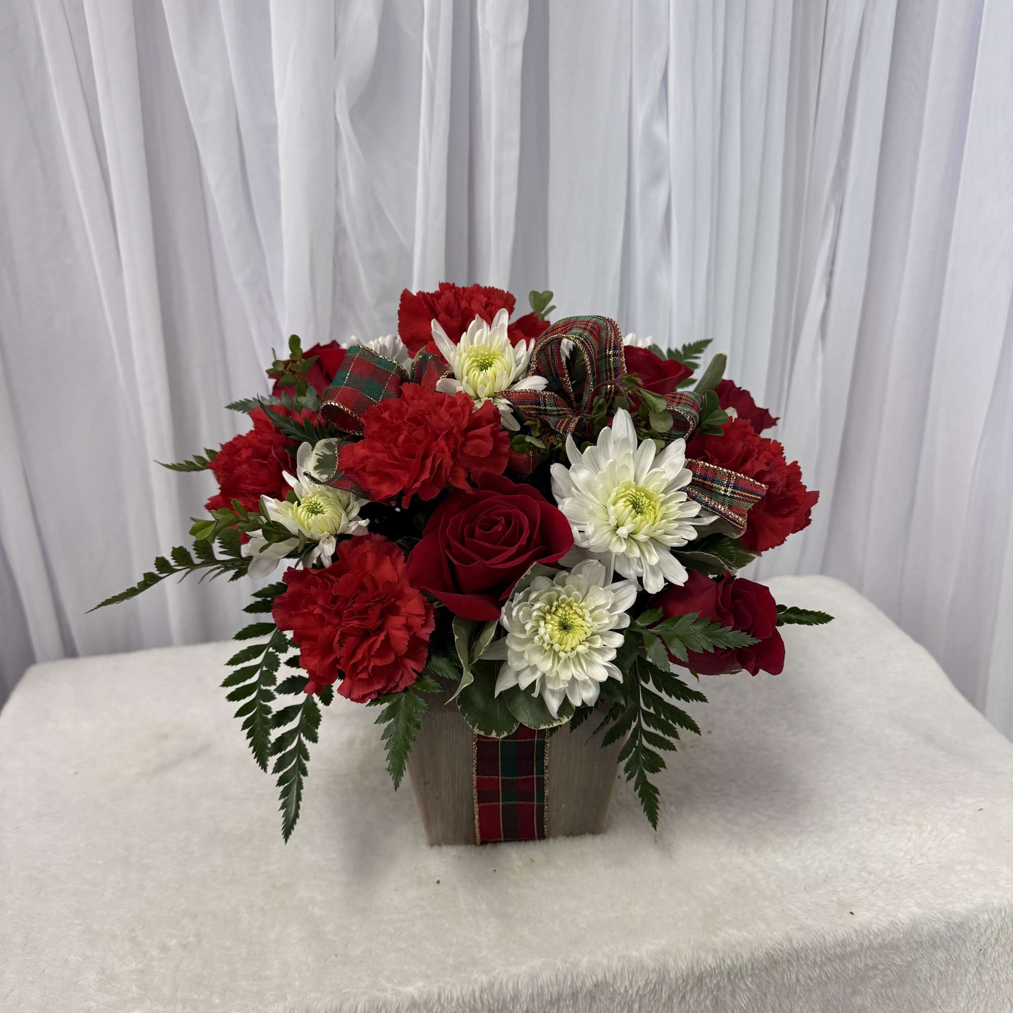 Red roses and white daisies in a square container with plaid ribbon
