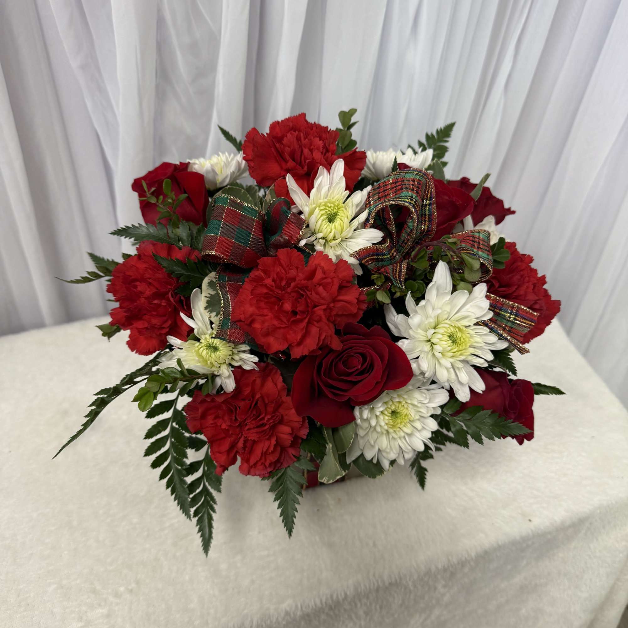 Red carnations and roses with white daisies in a low arrangement