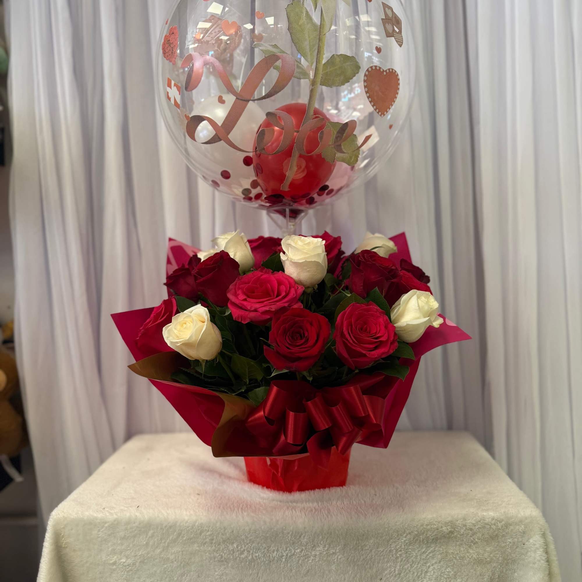 Red and white roses in red wrapping with a heart balloon above