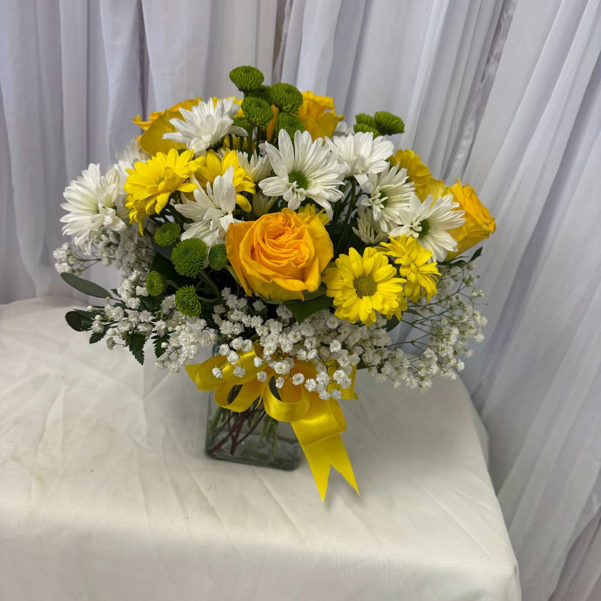 Yellow roses and white daisies in a glass vase with a yellow ribbon