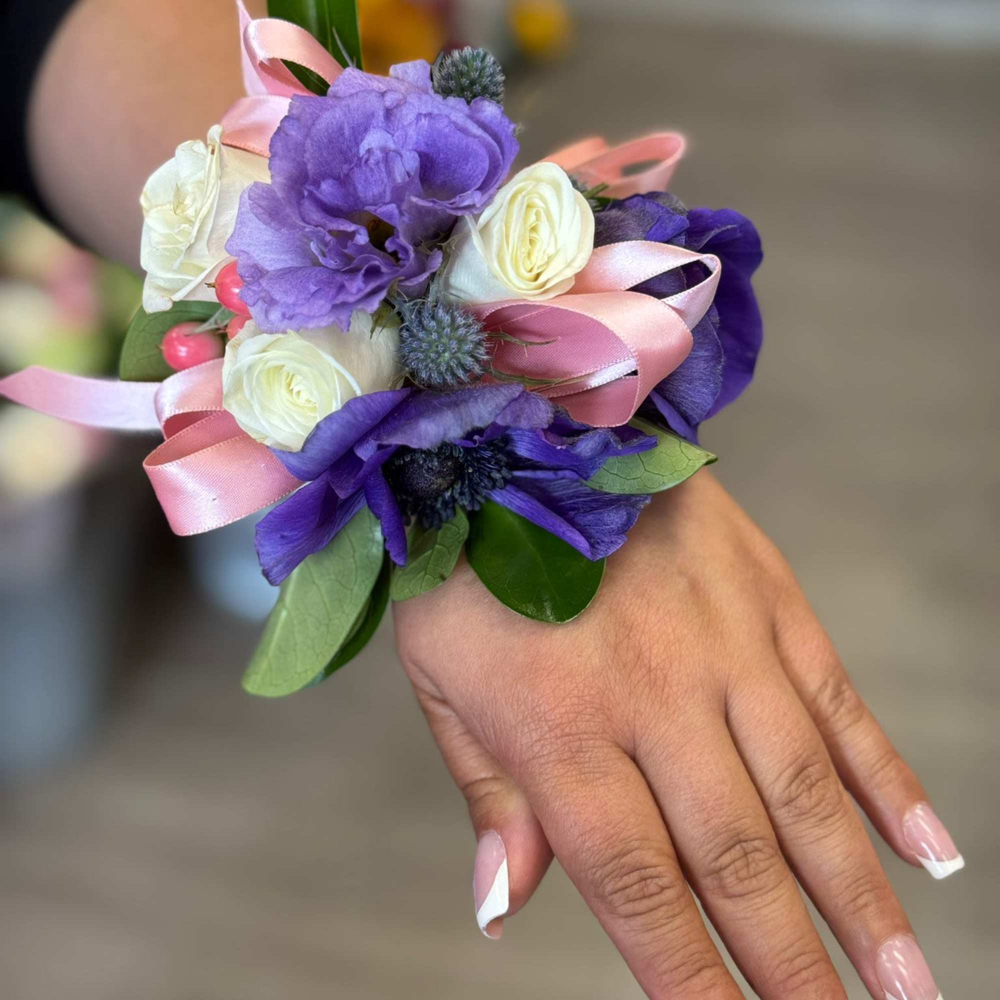 Purple and white wrist corsage with pink ribbon on a hand