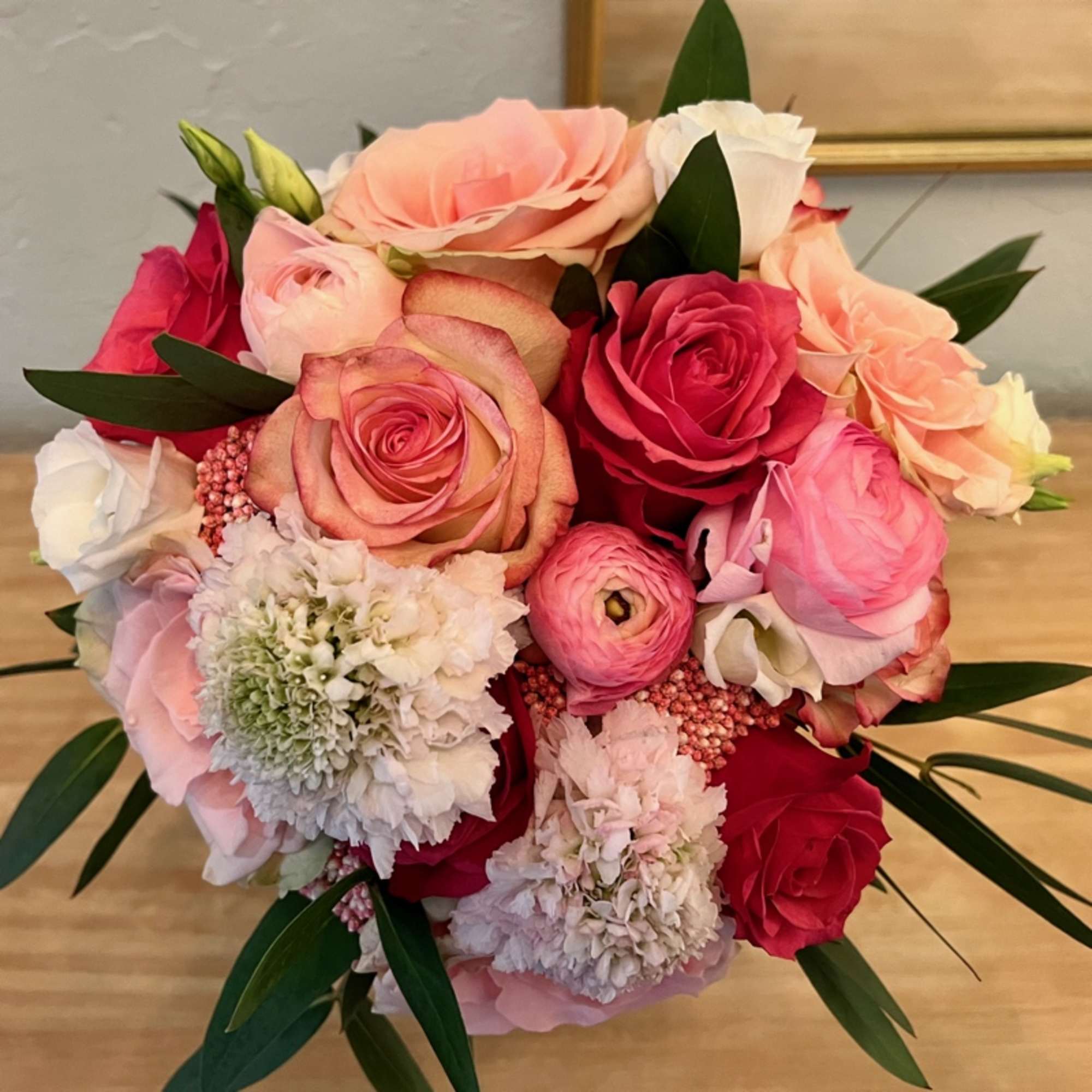 Tightly clustered bouquet of pink, peach, and white roses with round pink ranunculus blooms.