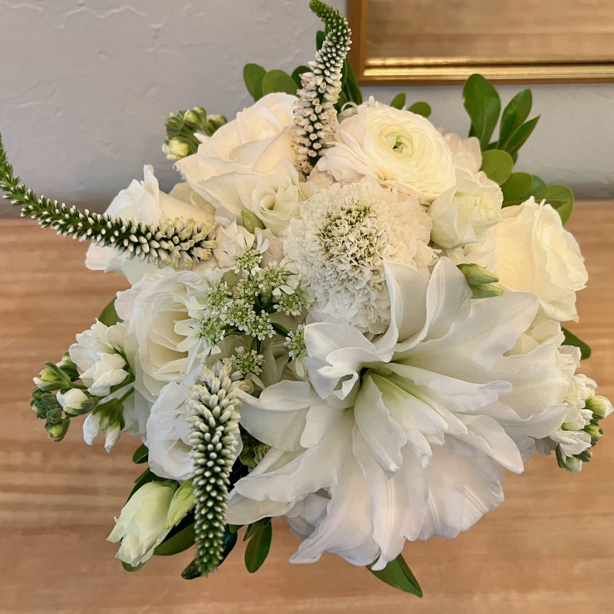 Compact all-white flower arrangement with roses, dahlias, and textured blooms in a rounded design