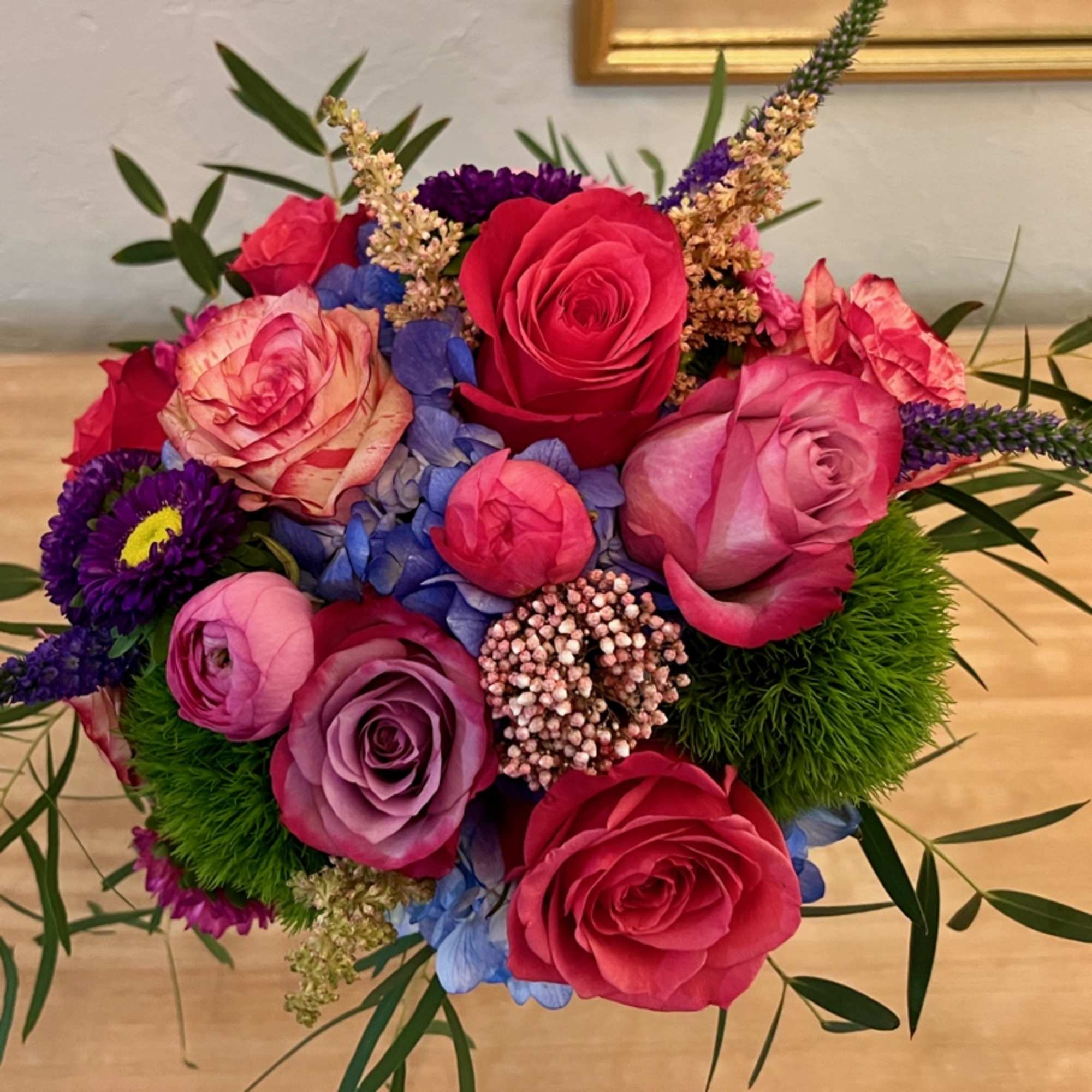 Vibrant mixed bouquet of pink roses, ranunculus, purple blooms, and blue hydrangea in a round arrangement