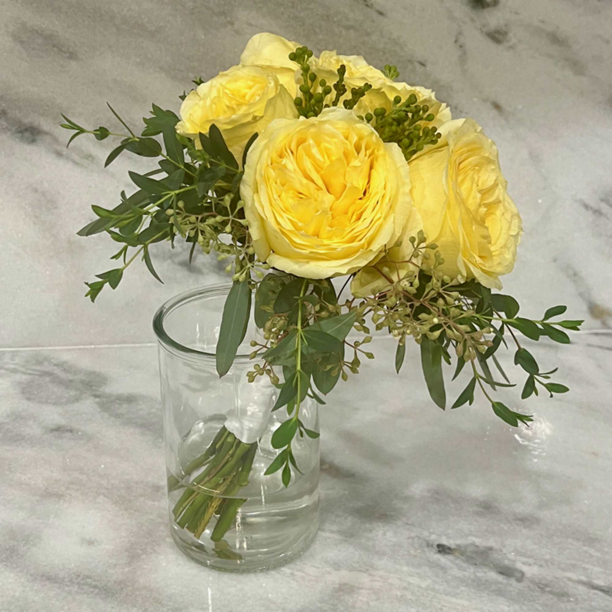 Yellow roses in a clear glass vase with greenery
