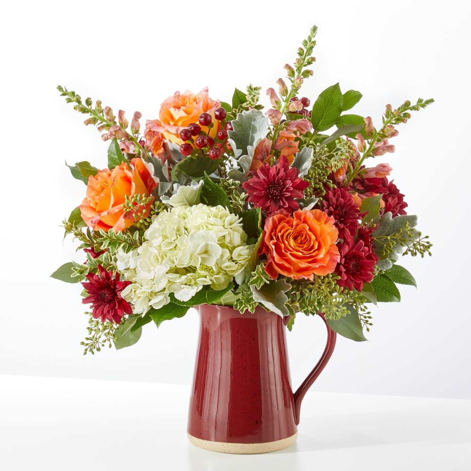 Bouquet of orange and burgundy flowers in a red ceramic pitcher