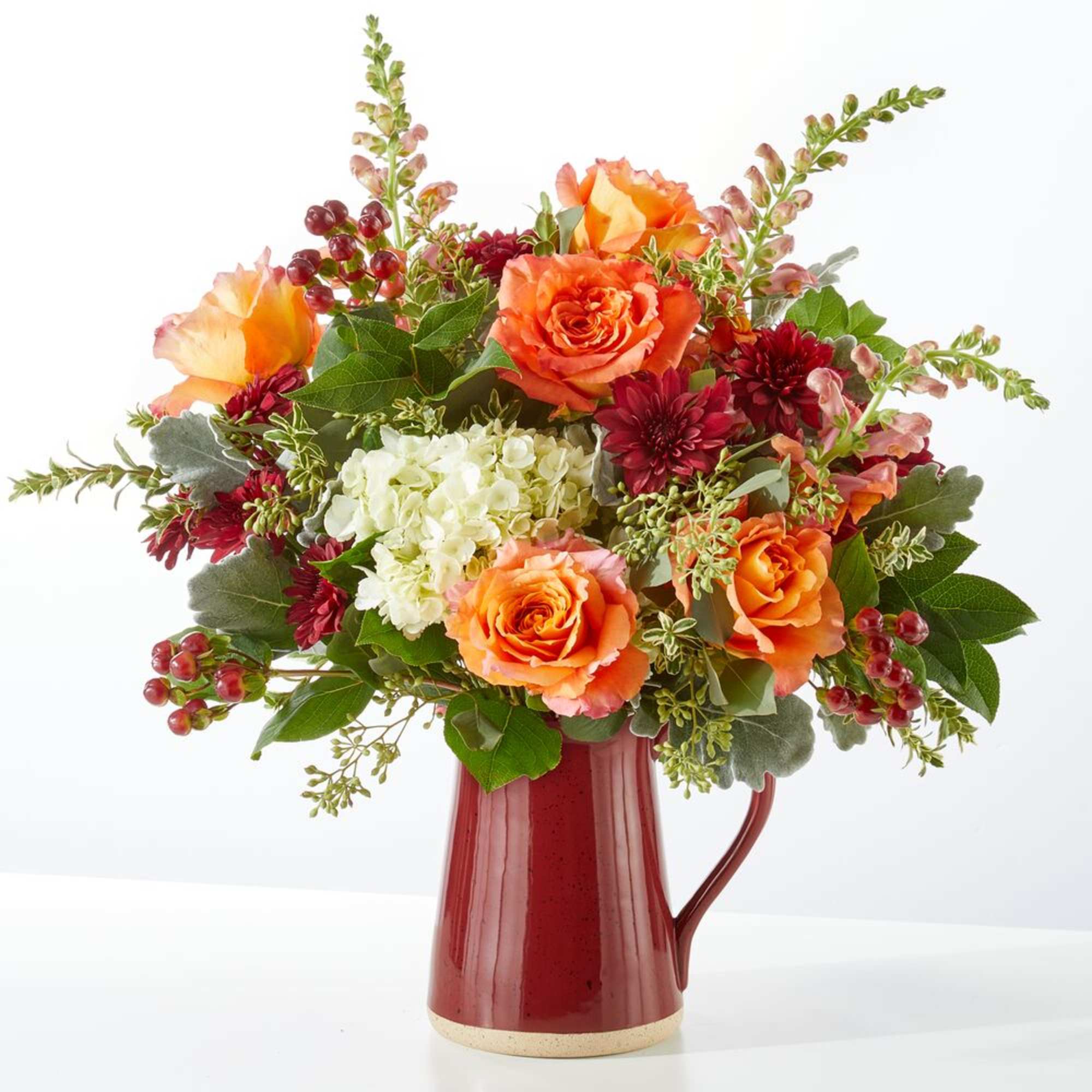 Orange roses and white hydrangea in a red pitcher vase