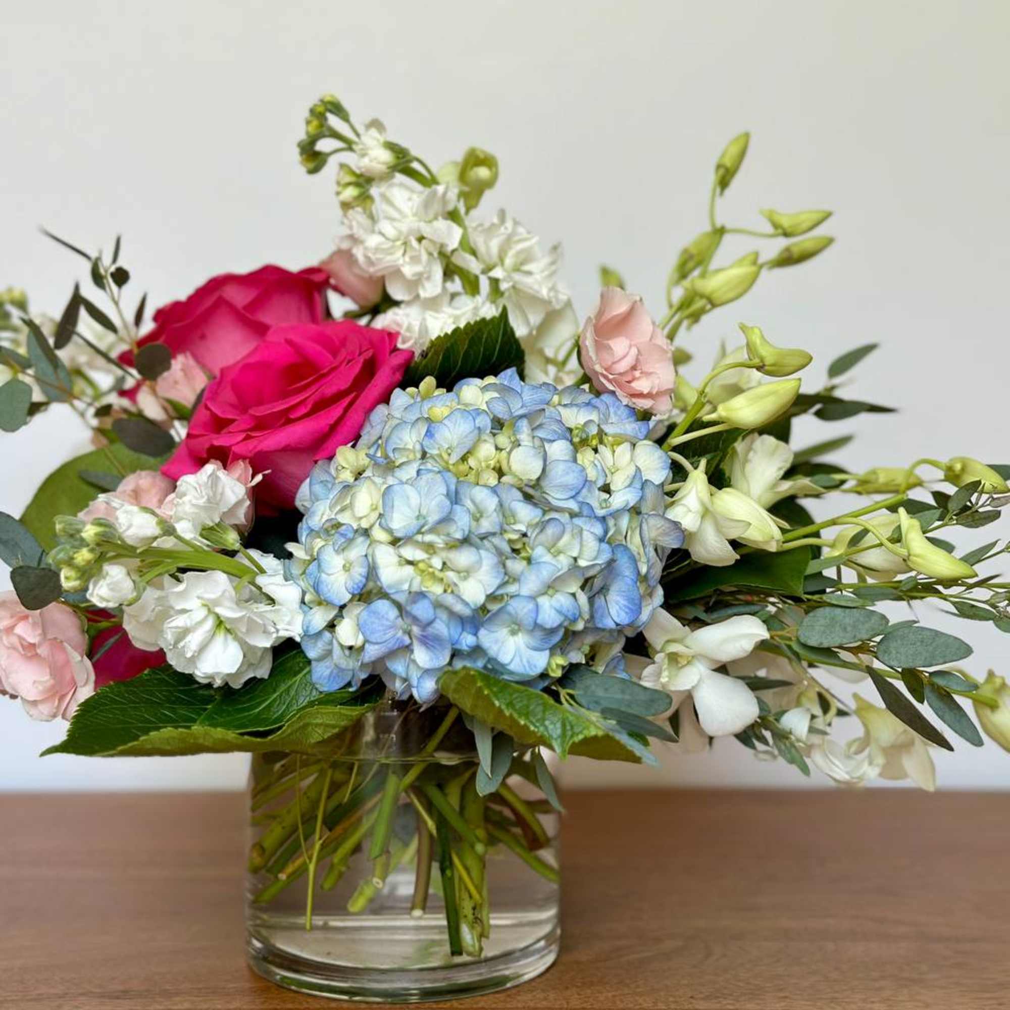 Mixed bouquet with pink roses, blue hydrangea, and white flowers in a glass vase