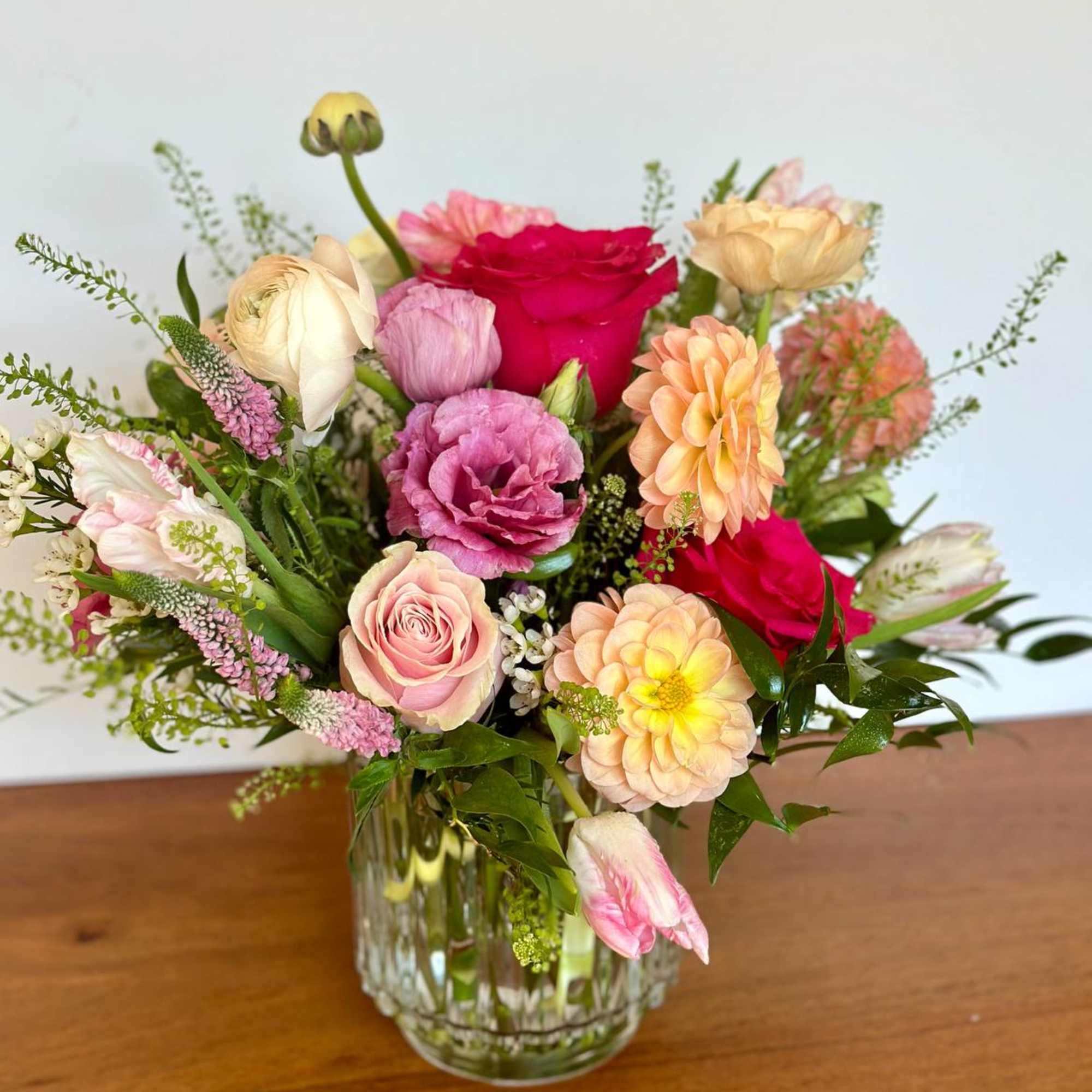 Mixed bouquet of pink, peach, and red flowers in a clear glass vase