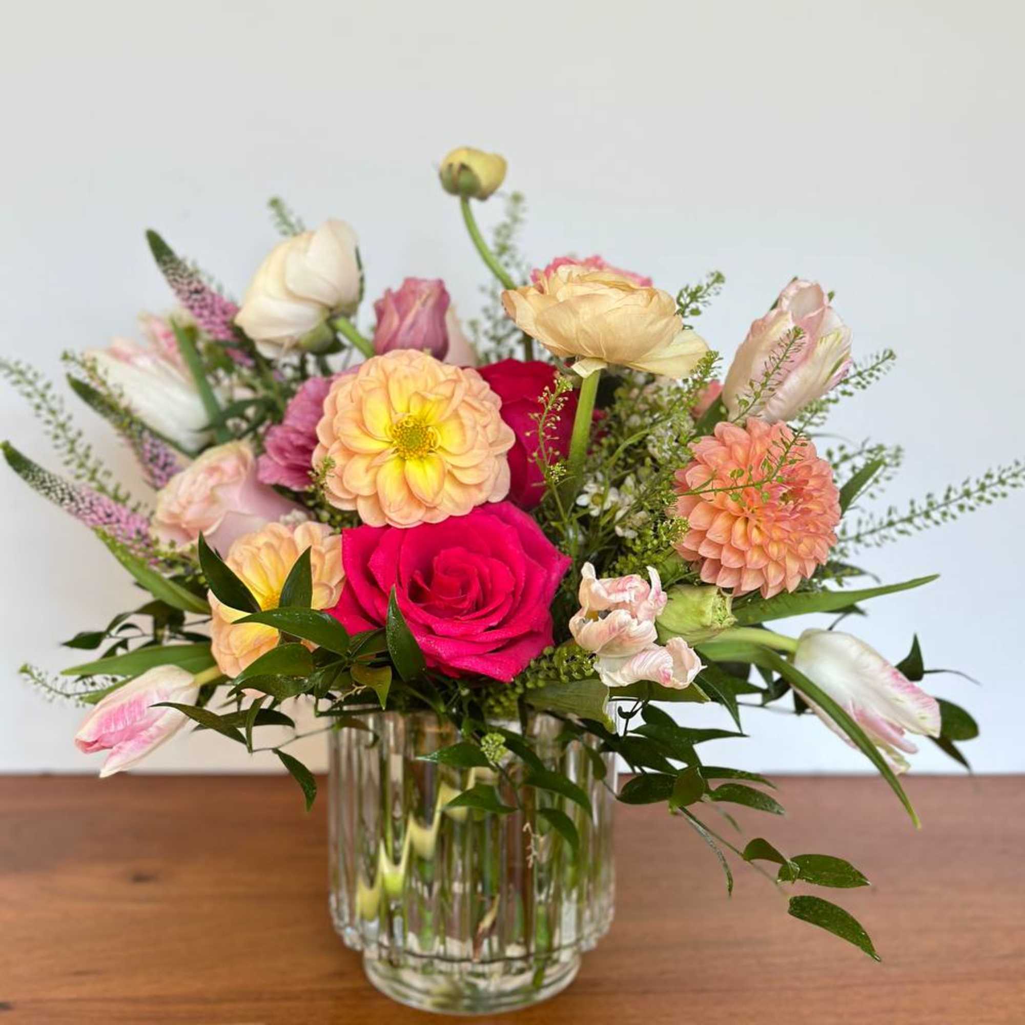 Mixed bouquet of roses, dahlias, and tulips in a clear glass vase