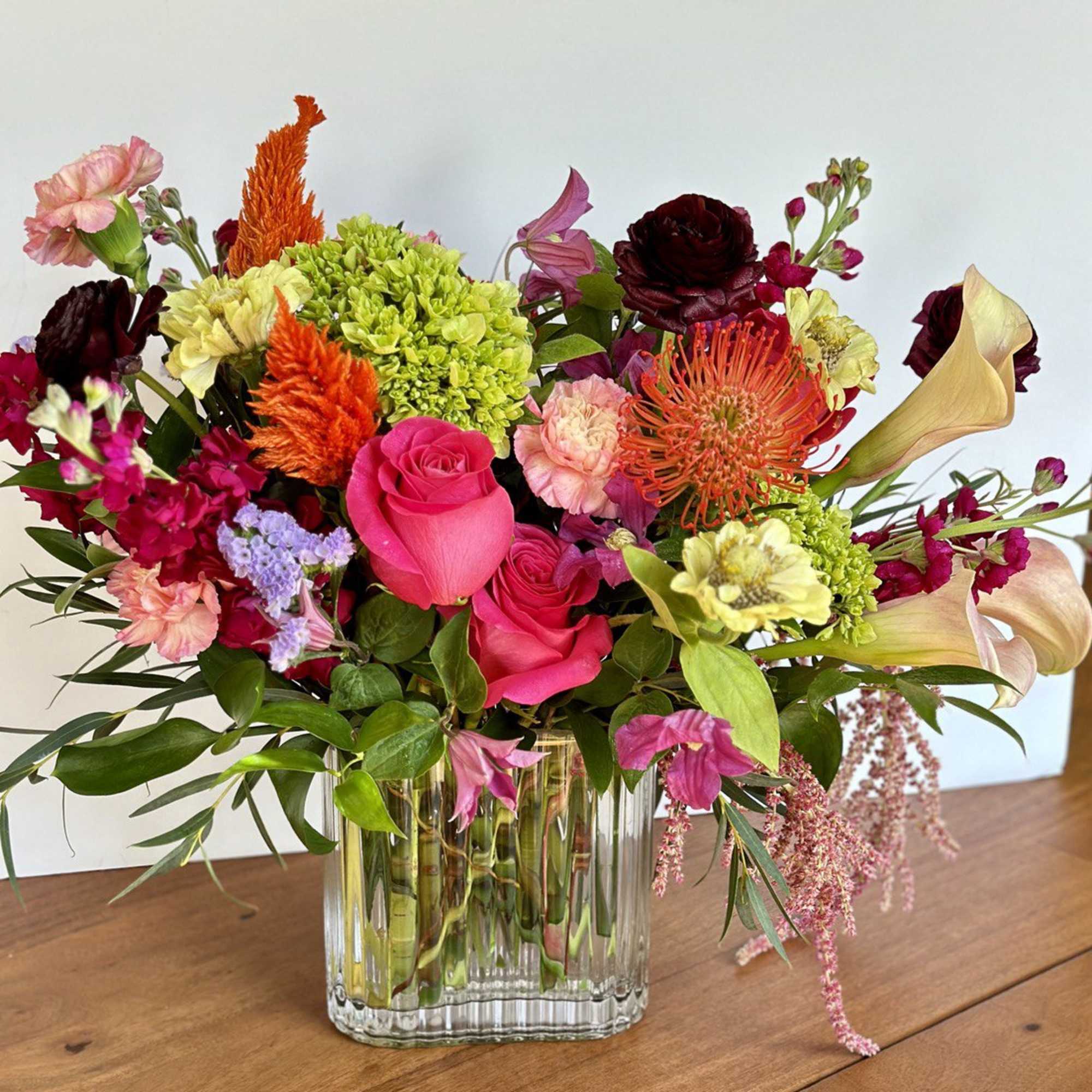 Mixed bouquet of pink, orange, and green flowers in a clear glass vase