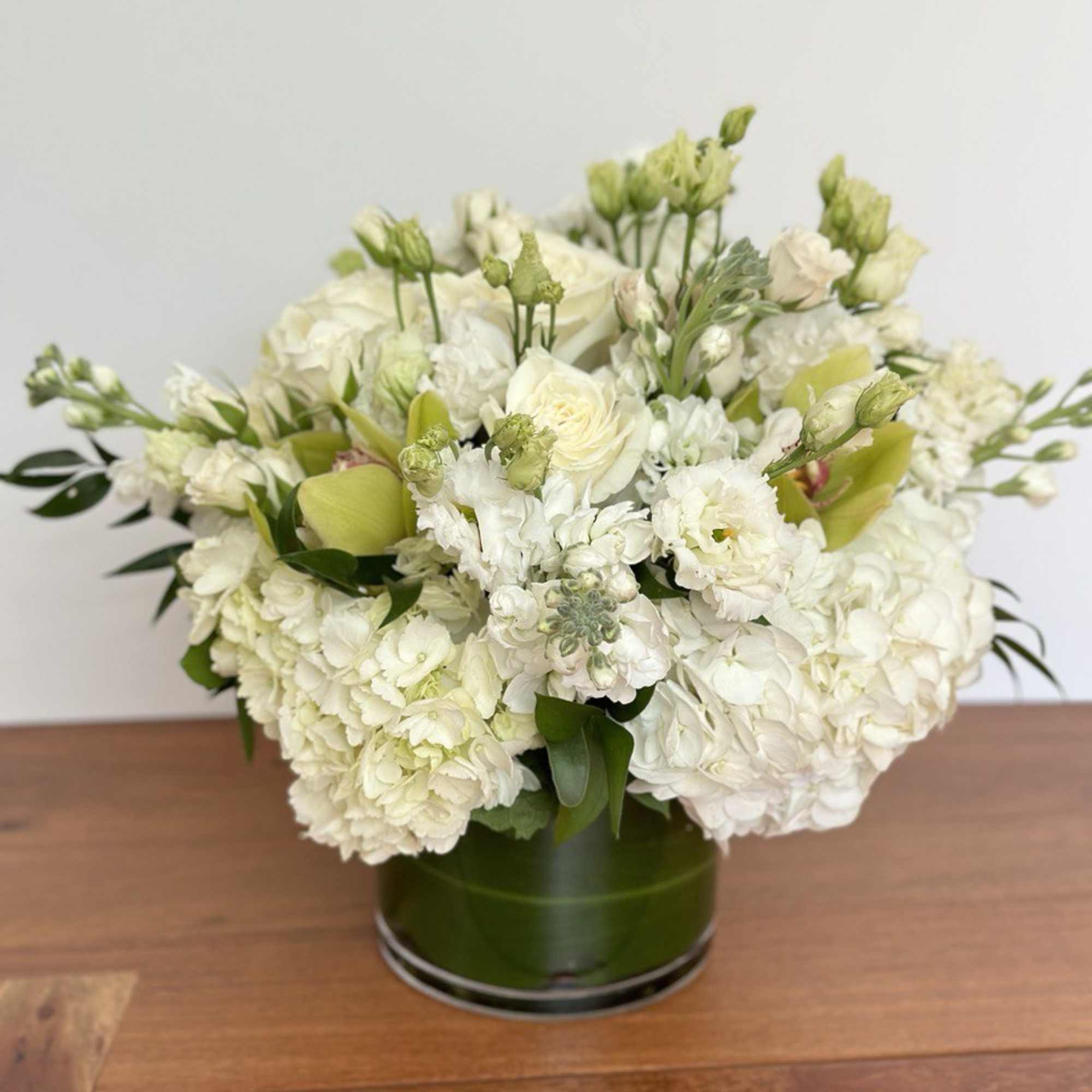 White floral arrangement in a green glass vase on a wooden table